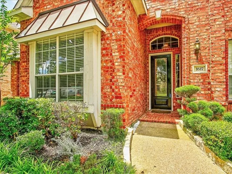 Red brick facade with a black front door, arched transom window, and a bay window featuring a metal awning