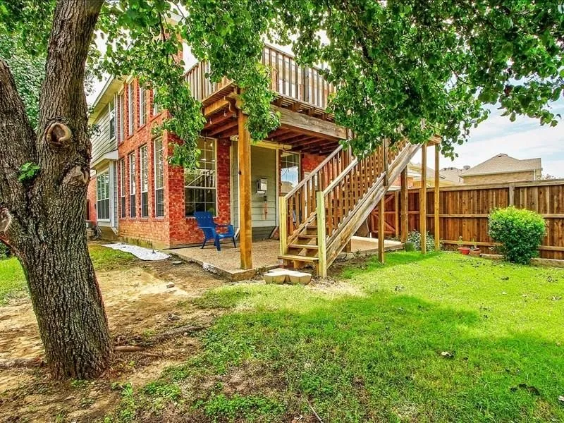 Brick exterior with multiple windows, second-story balcony, ground-level patio, and wood privacy fence