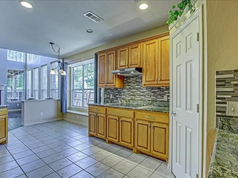Tile flooring, wood cabinetry, stone countertops, mosaic tile backsplash, and recessed lighting