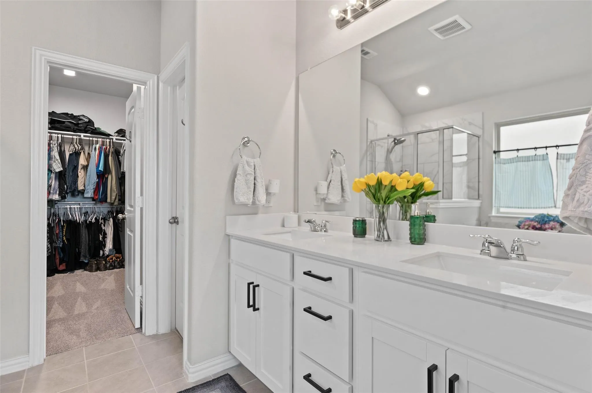 Dual sink vanity with white countertops, chrome fixtures, and black cabinet hardware