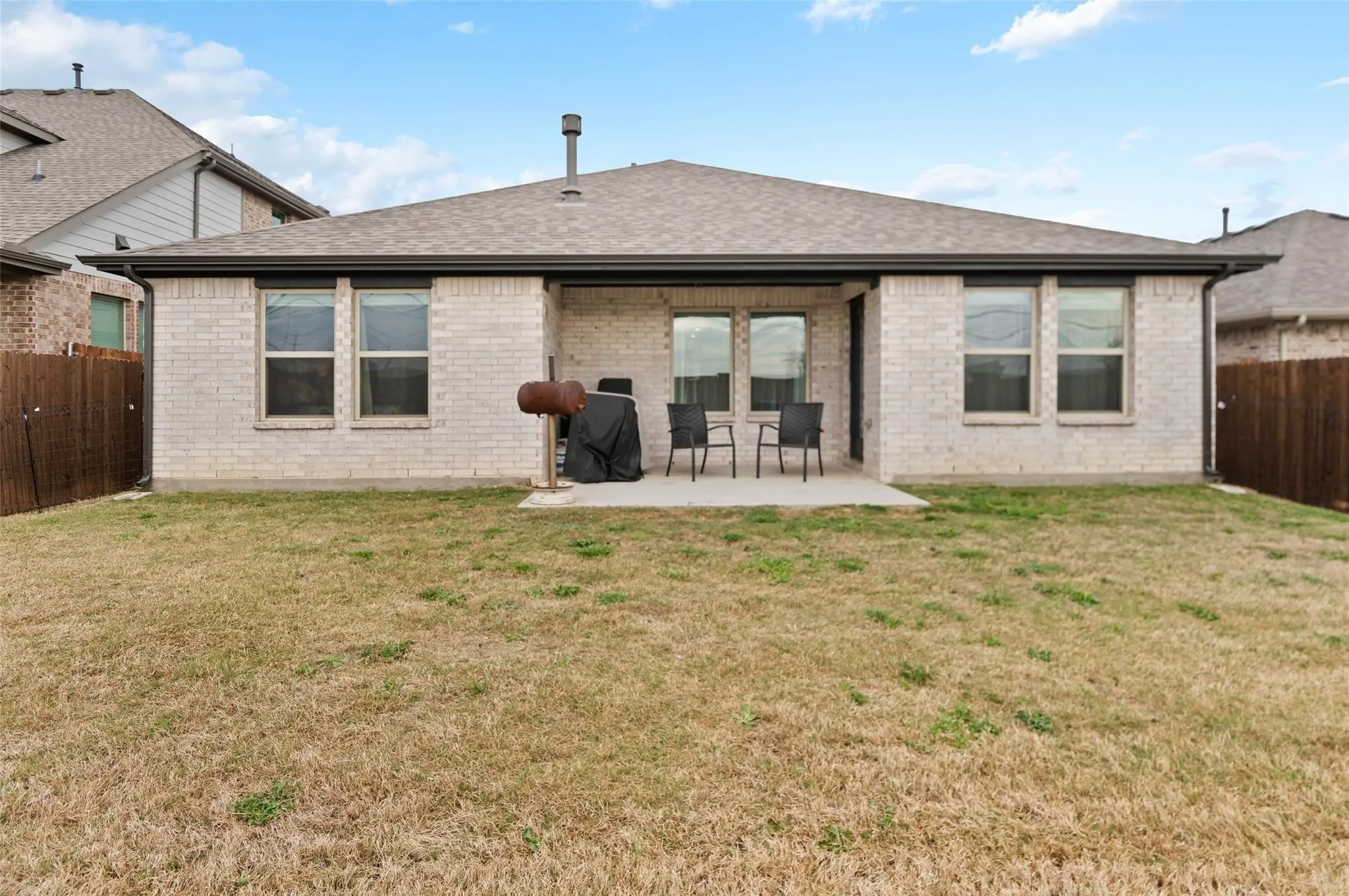 Brick exterior with a covered patio, multiple windows, and a fenced perimeter