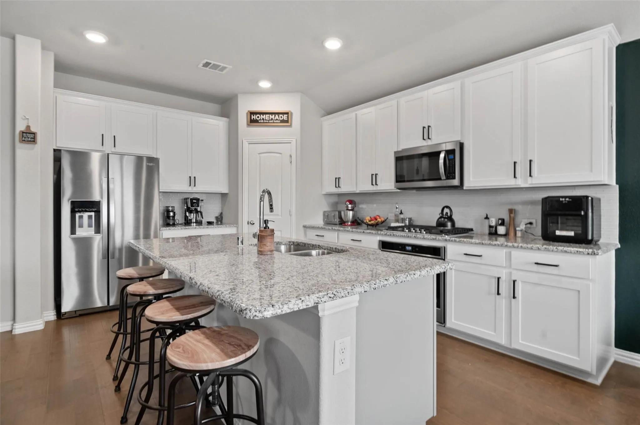 Kitchen featuring white cabinetry, stainless steel appliances, a center island with a built-in sink, wood-finish flooring, and recessed lighting