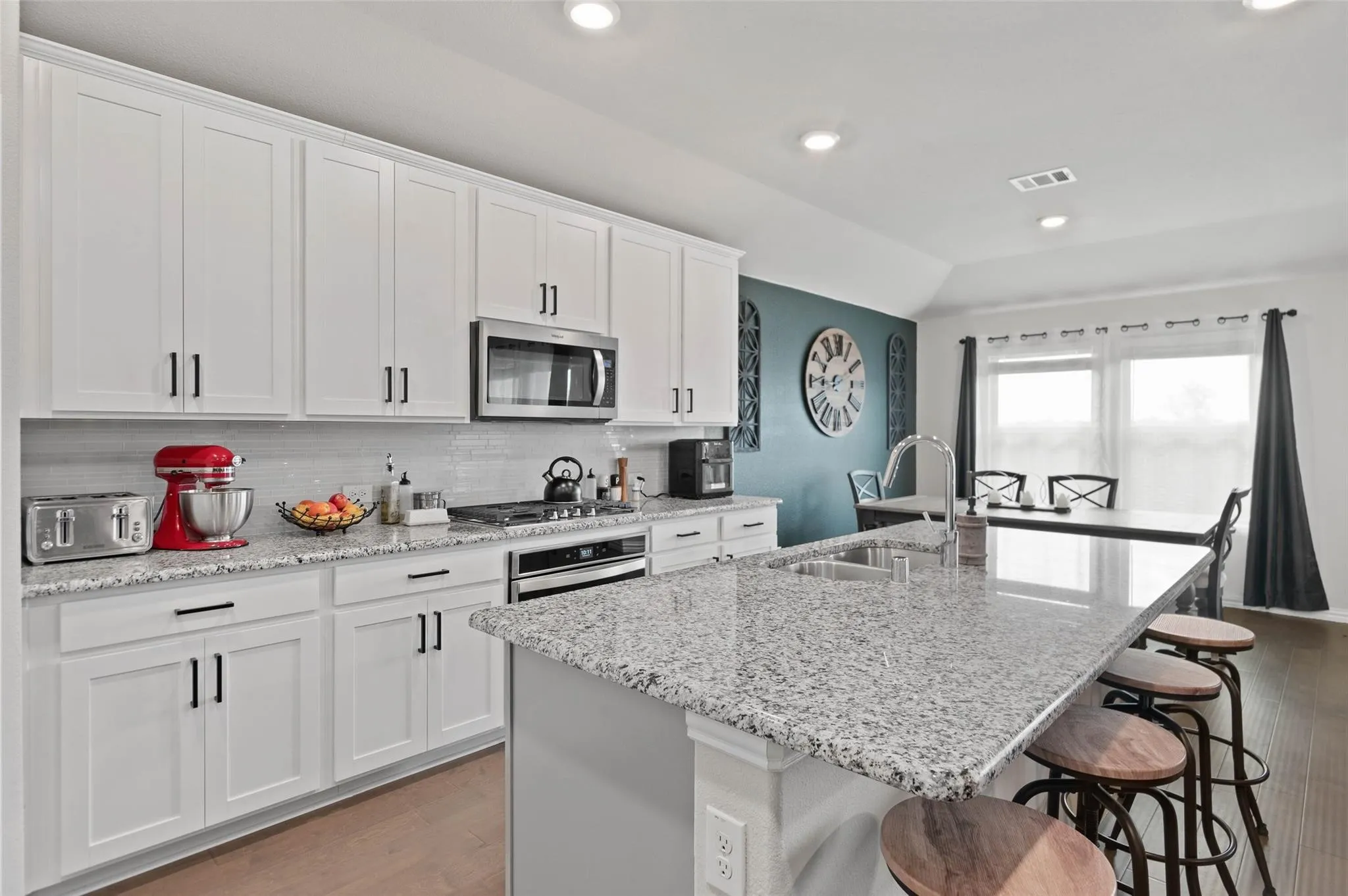White cabinetry with dark hardware, granite countertops, stainless steel appliances, wood-finish flooring, and recessed lighting