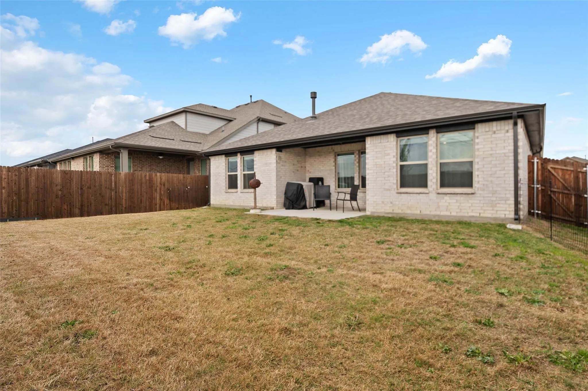 Brick exterior with a shingled roof, a concrete patio, and a wood privacy fence
