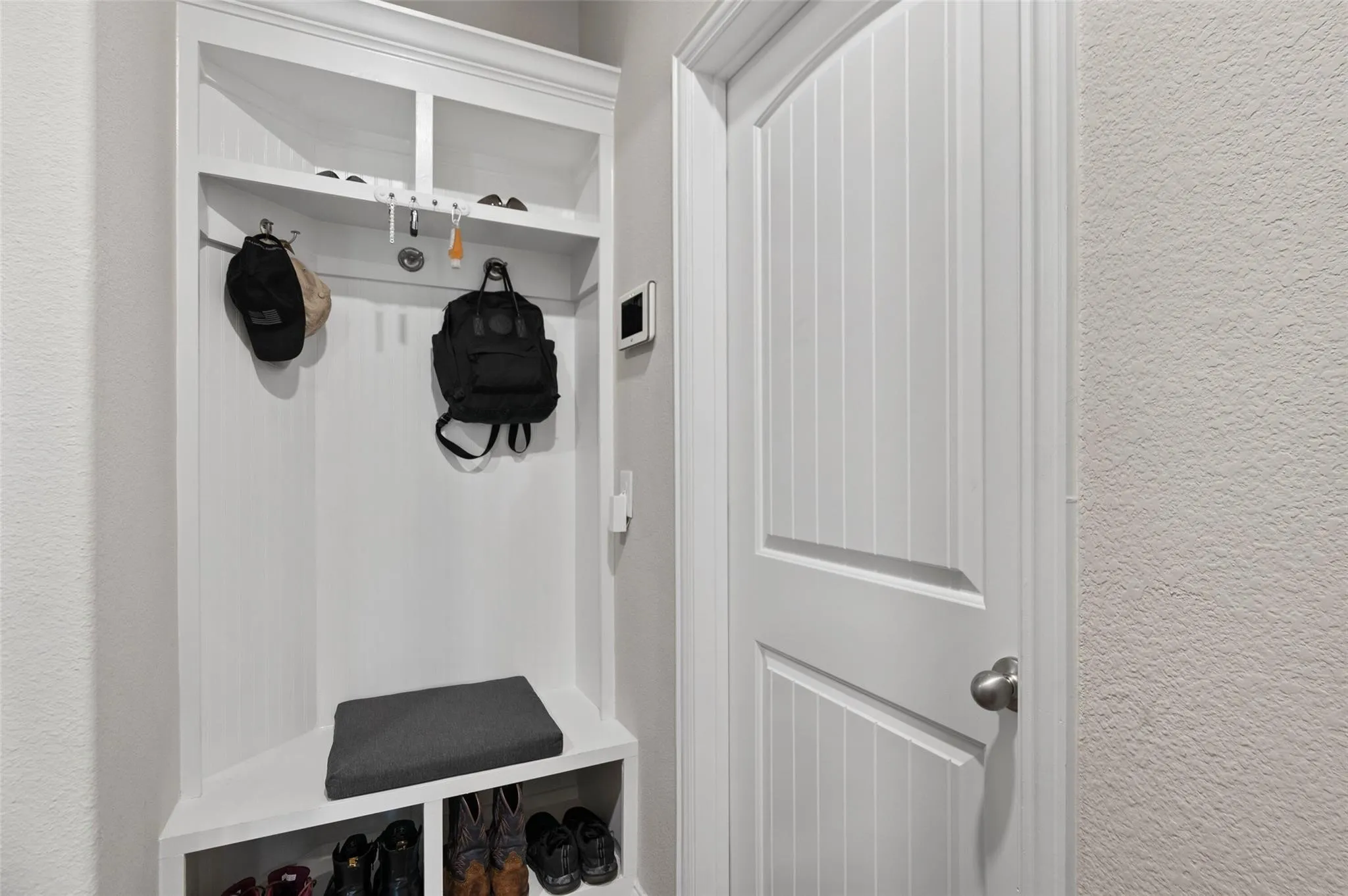Built-in storage bench with shelving and hooks, beadboard paneling, and a paneled white door