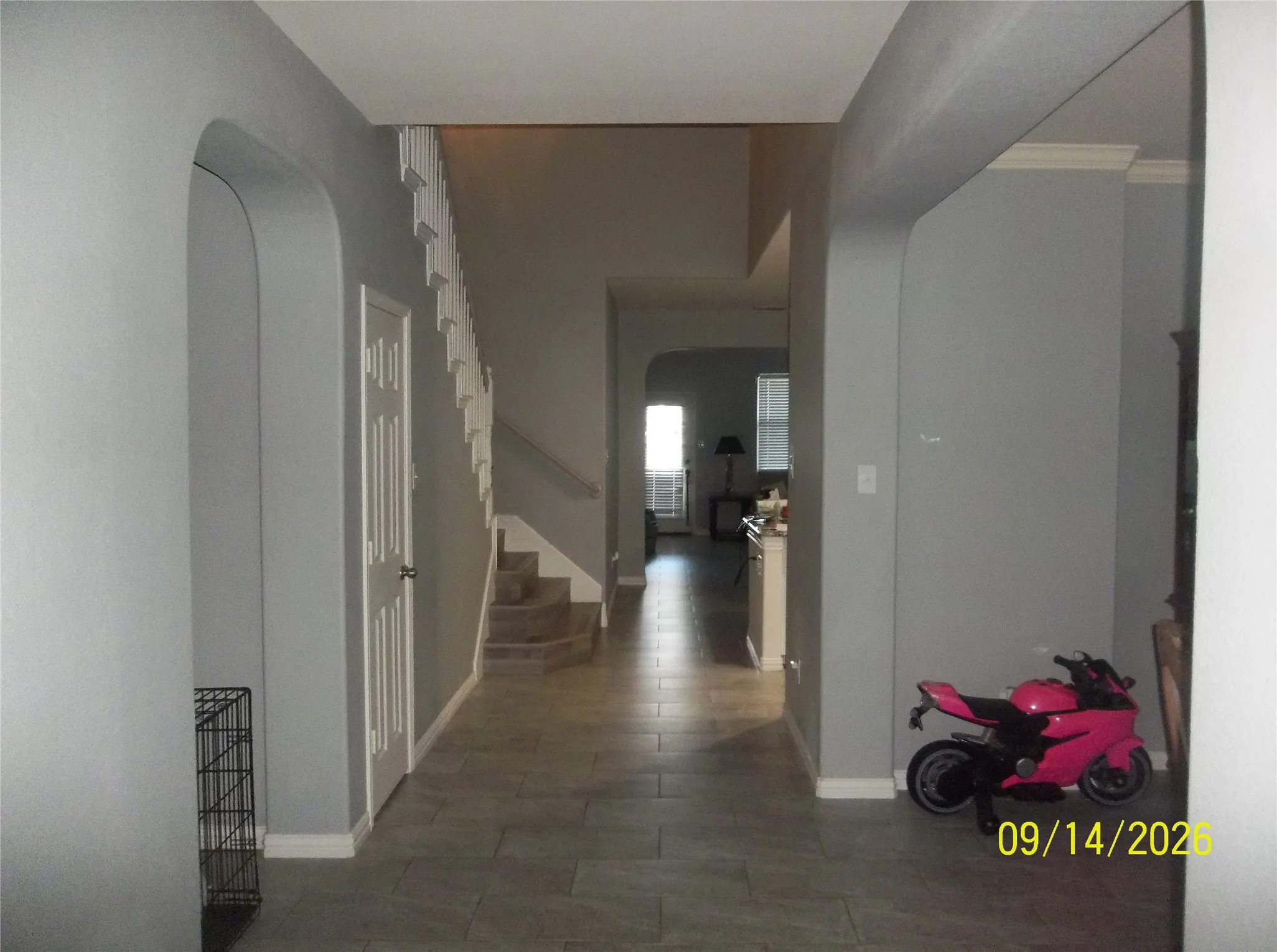 Spacious hallway featuring archway openings, tile flooring, a staircase with white risers, and a white paneled door