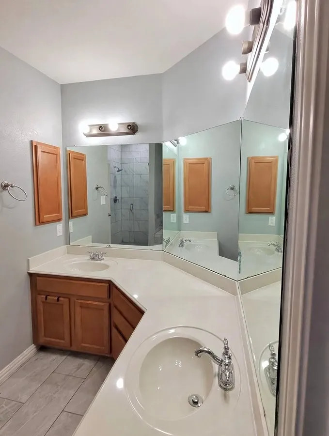 Dual vanity with light countertops, wood-finish cabinetry, built-in medicine cabinets, and tile flooring