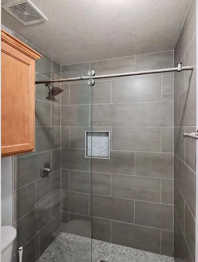 Shower with gray rectangular tile walls, built-in storage niche, glass enclosure, and a rain-style showerhead