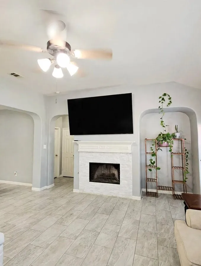 Wood-finish tile flooring throughout, fireplace with a decorative mantel, ceiling fan with integrated lighting, and arched wall alcoves