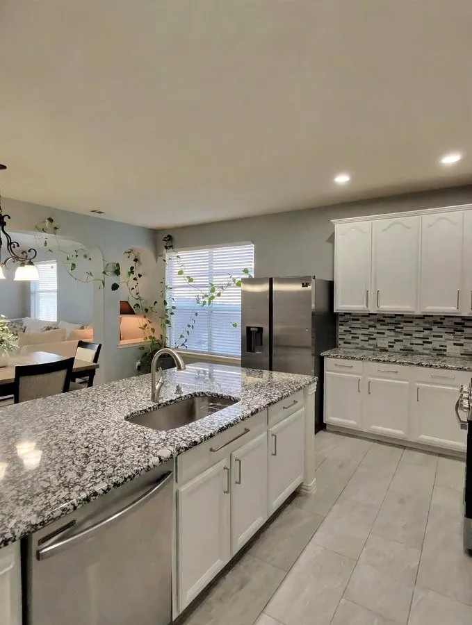Kitchen featuring a stainless steel refrigerator, white cabinetry, a large kitchen island with an undermount sink, granite countertops, and tile flooring
