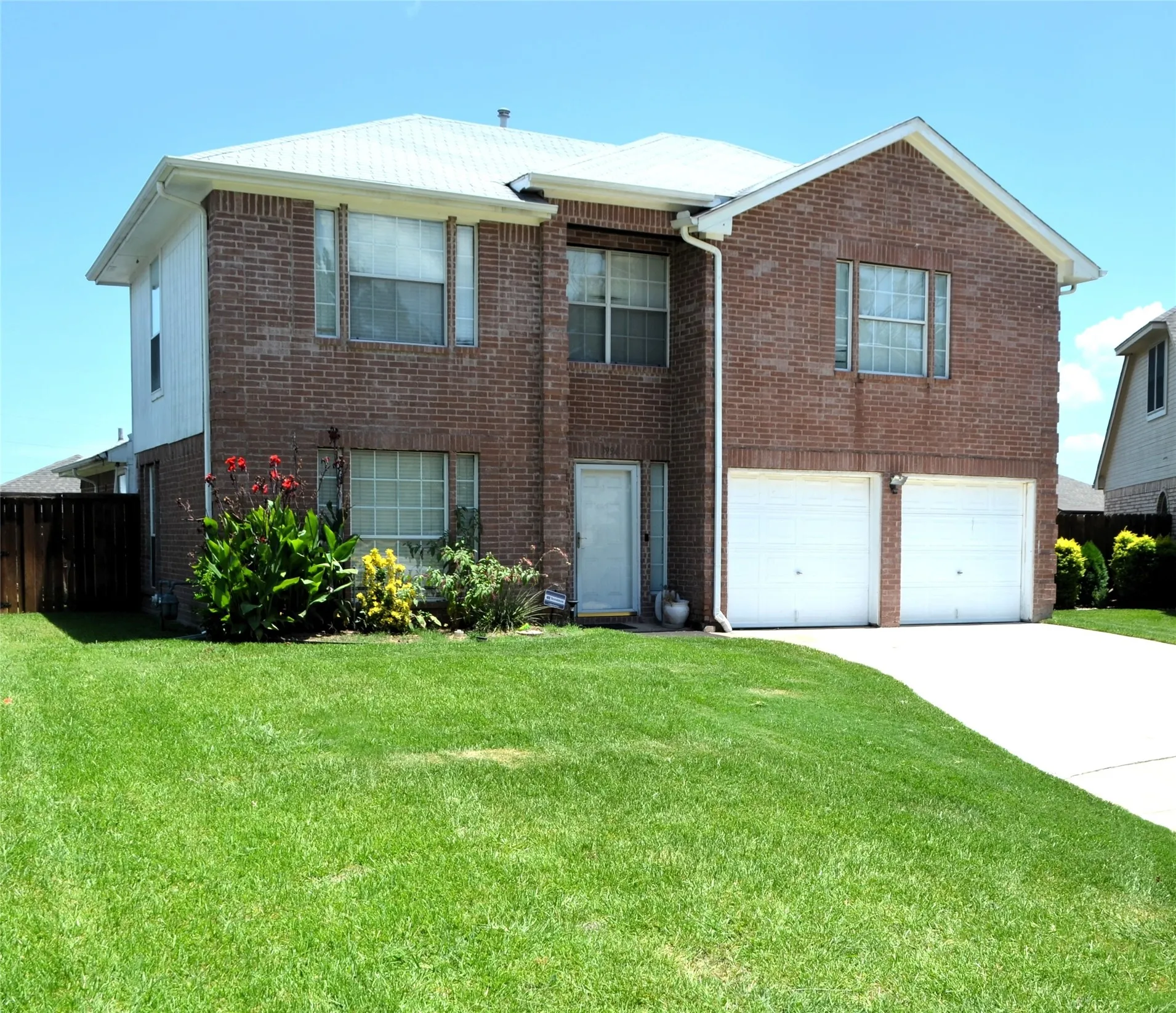 Brick exterior with white siding accents, a two-car garage, a white entry door, and mature landscaping
