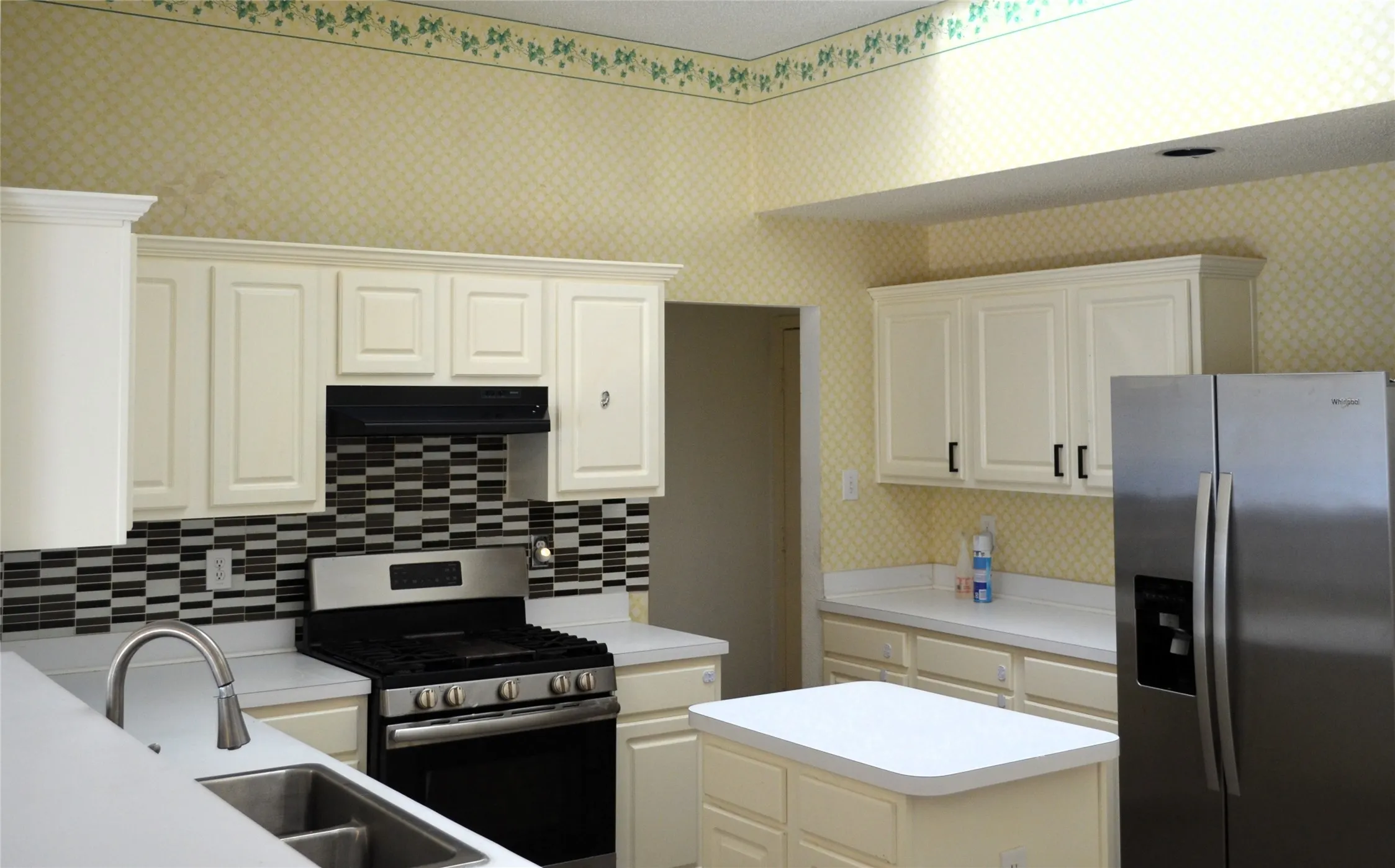 Kitchen featuring white paneled cabinetry, stainless steel appliances, a center island, a black and white mosaic tile backsplash, and a double basin sink with a gooseneck faucet