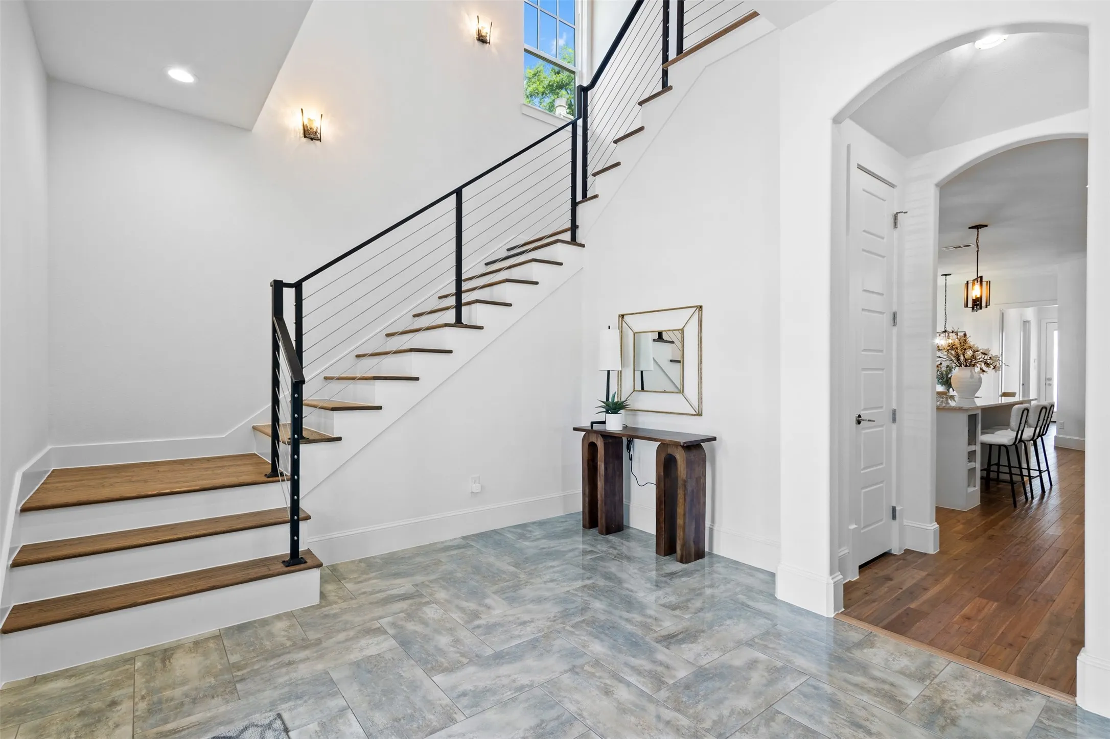 Herringbone tile flooring, wood-finish staircase with contemporary cable railing, arched doorway, recessed lighting, and wall sconces