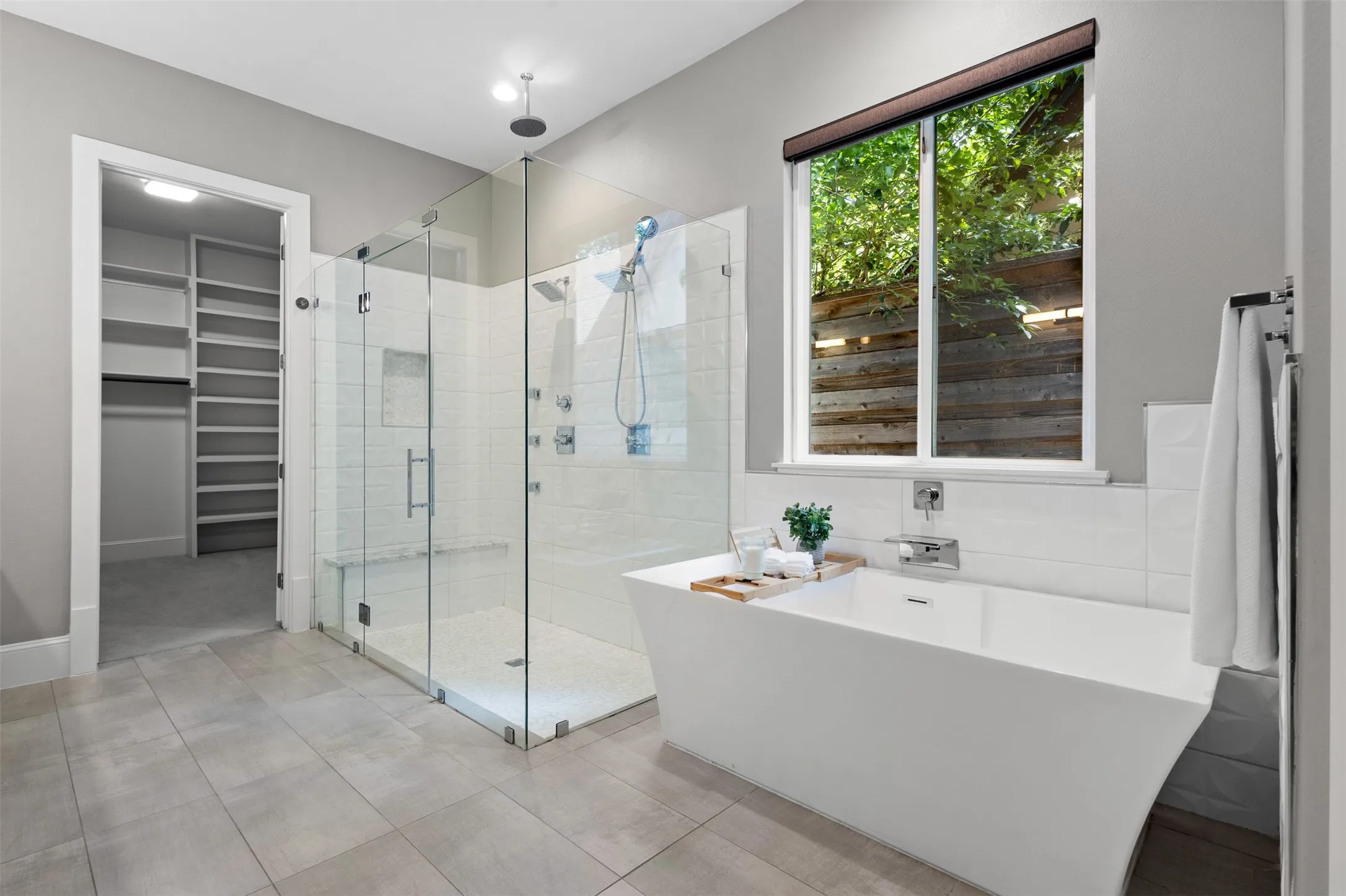Freestanding soaking tub, glass-enclosed shower with tiled bench, and a custom walk-in closet featuring extensive shelving