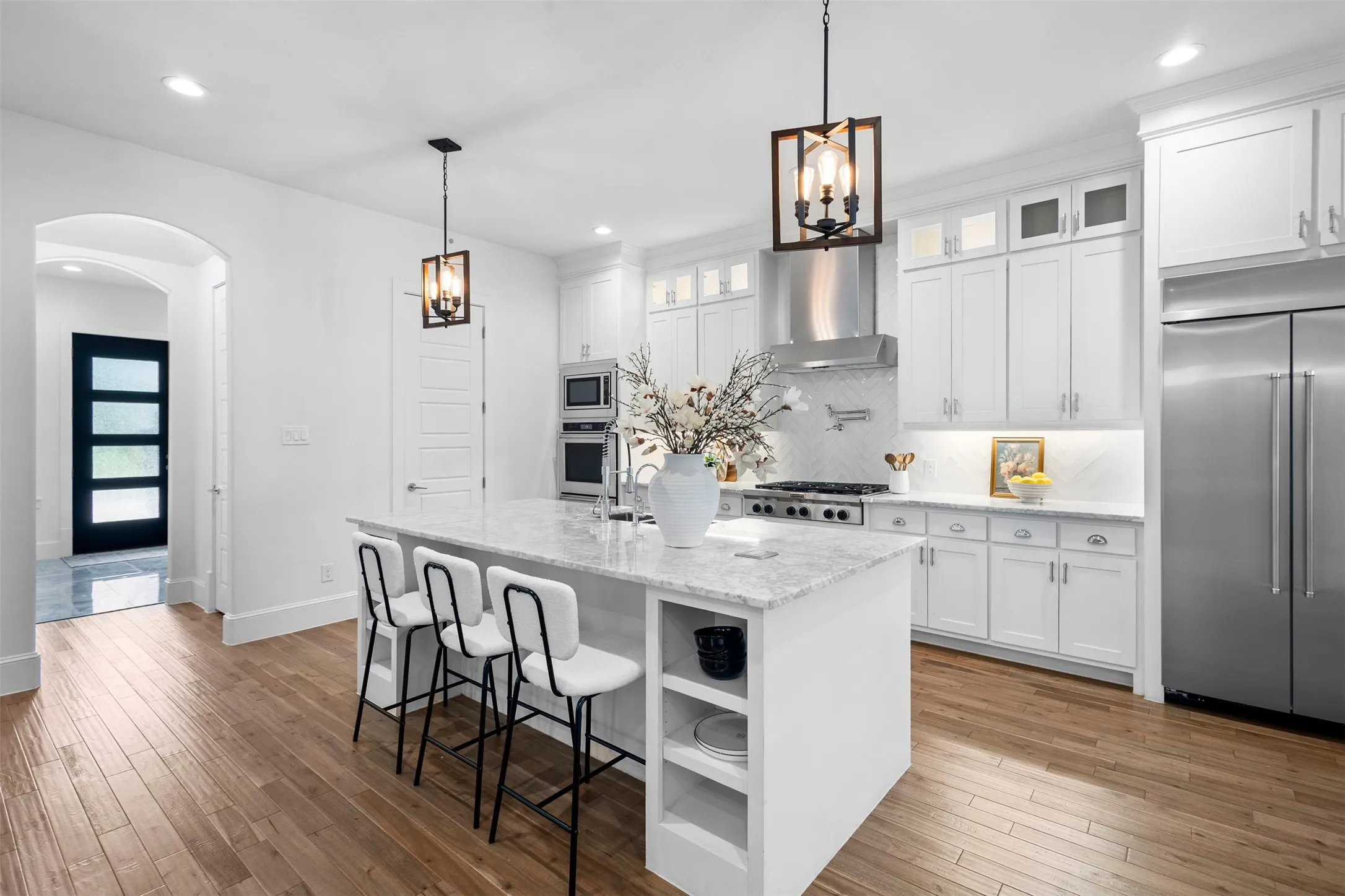 Spacious kitchen featuring an expansive center island with seating, a professional-grade range, stainless steel appliances, white cabinetry, and wood-finish flooring