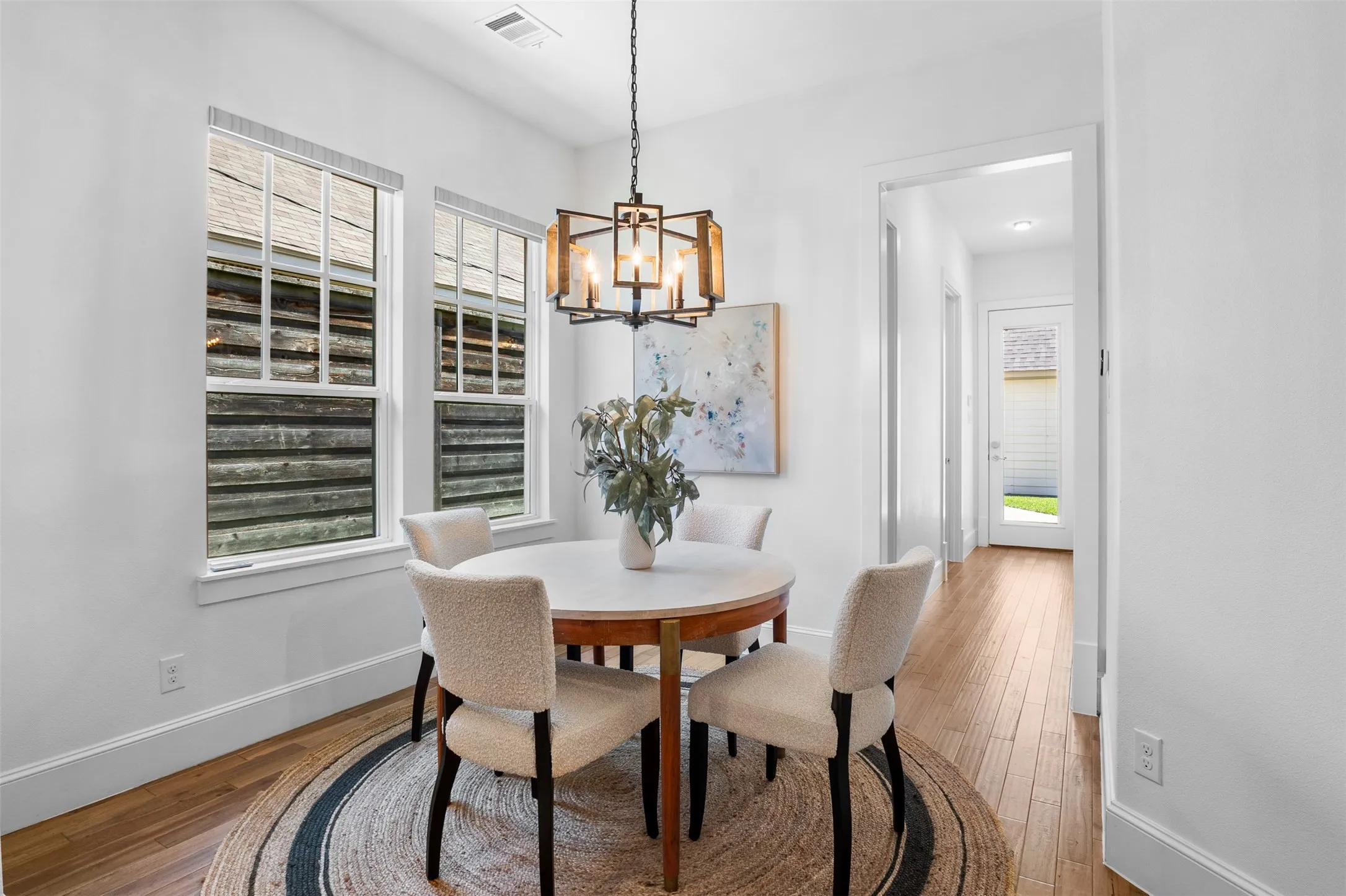 Bright dining space featuring wood-finish flooring, a contemporary chandelier, and multiple windows with blinds