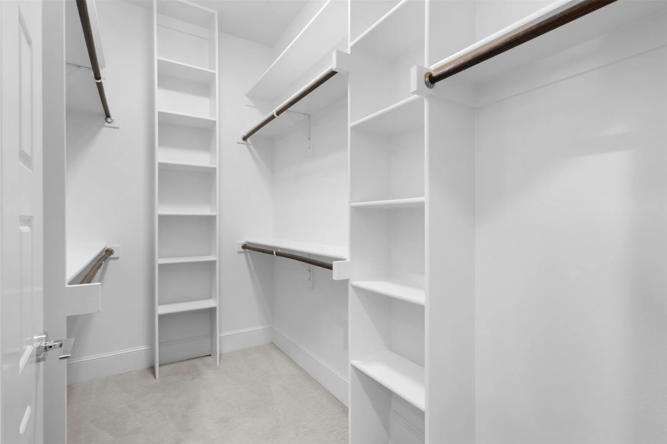 Walk-in closet with extensive built-in shelving, multiple hanging rods, white-finish cabinetry, and soft carpeting