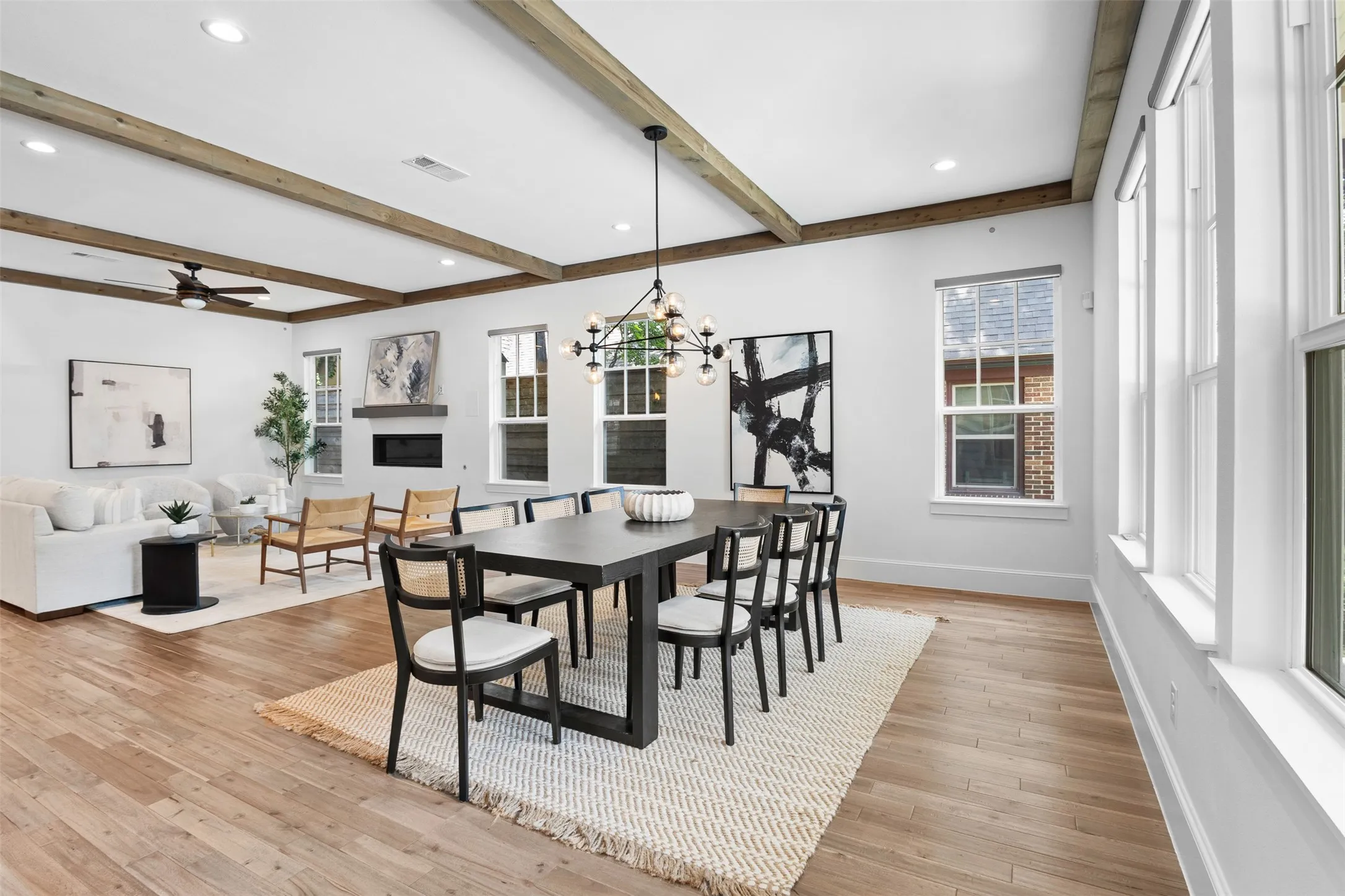 Open-concept living and dining area featuring wood-finish flooring, exposed ceiling beams, recessed lighting, and multiple windows