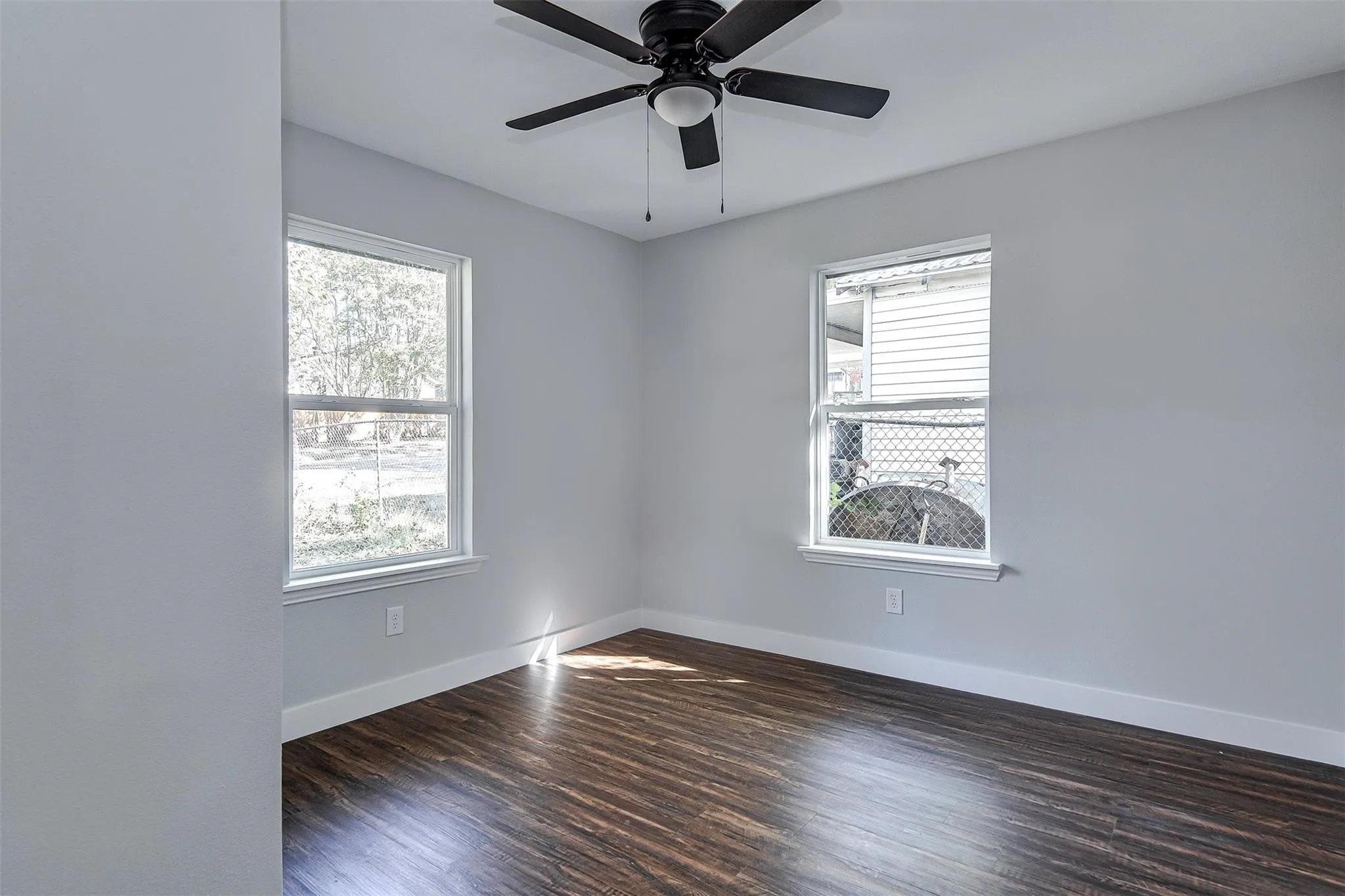 Wood-finish flooring, two large windows, a ceiling fan with integrated lighting, and light-colored walls