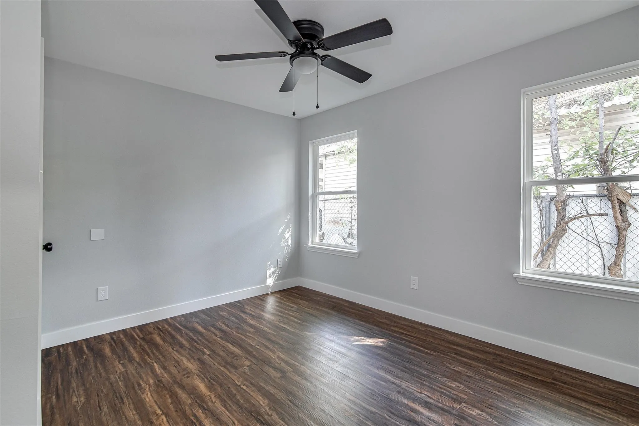 Wood-finish flooring with white trim, light gray walls, and two windows