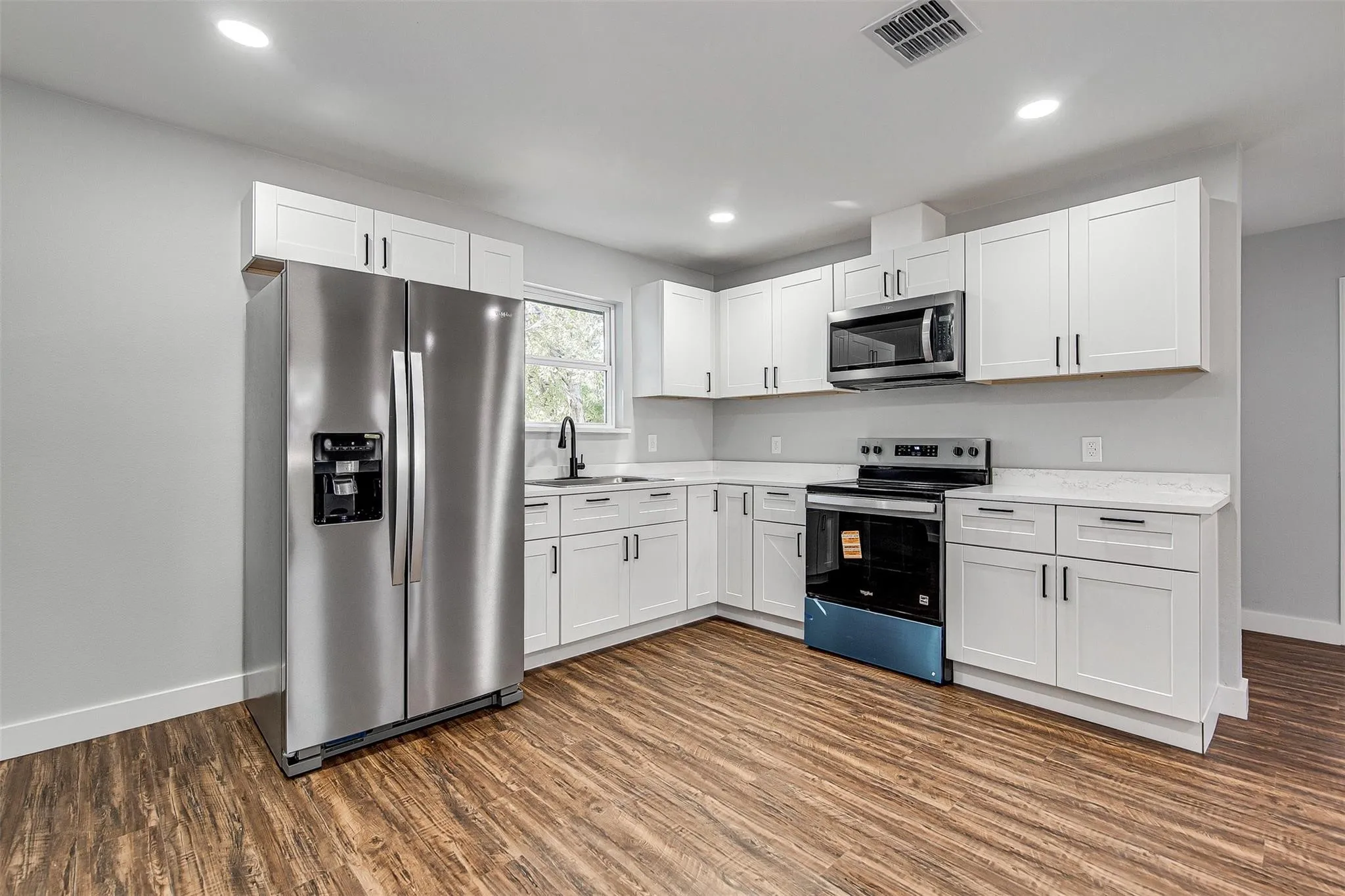 Kitchen featuring wood-finish flooring, white cabinetry with dark hardware, stainless steel appliances, and light-toned countertops