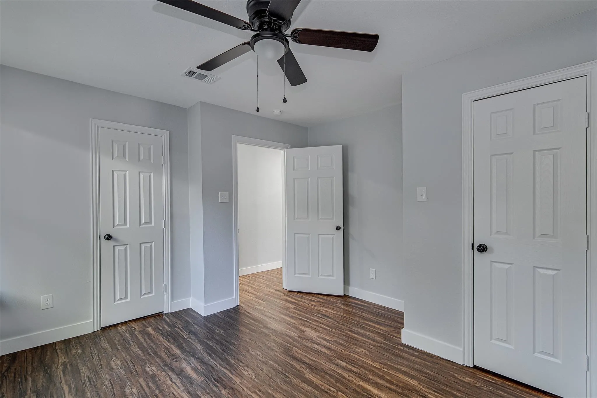Wood-finish flooring, white paneled doors, ceiling fan with light fixture, and light gray wall paint
