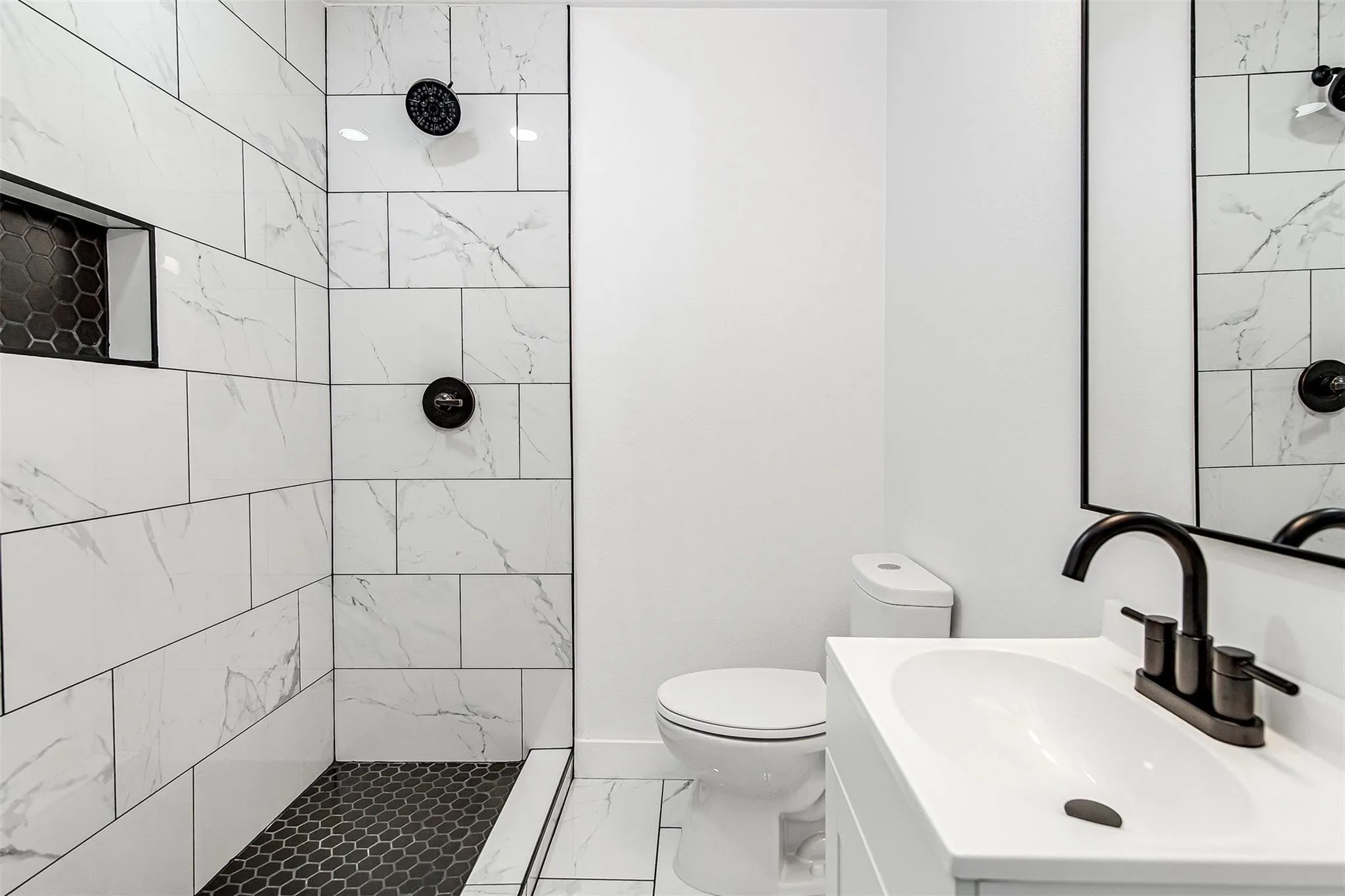 Shower with white tile surround, dark hexagonal tile floor, and built-in niche