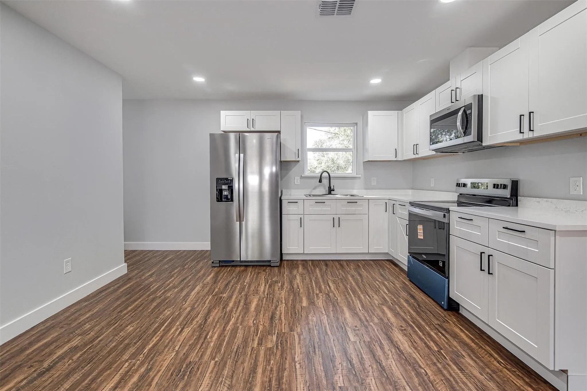 Kitchen featuring wood-finish flooring, white cabinetry, a stainless steel refrigerator, white countertops, and recessed lighting