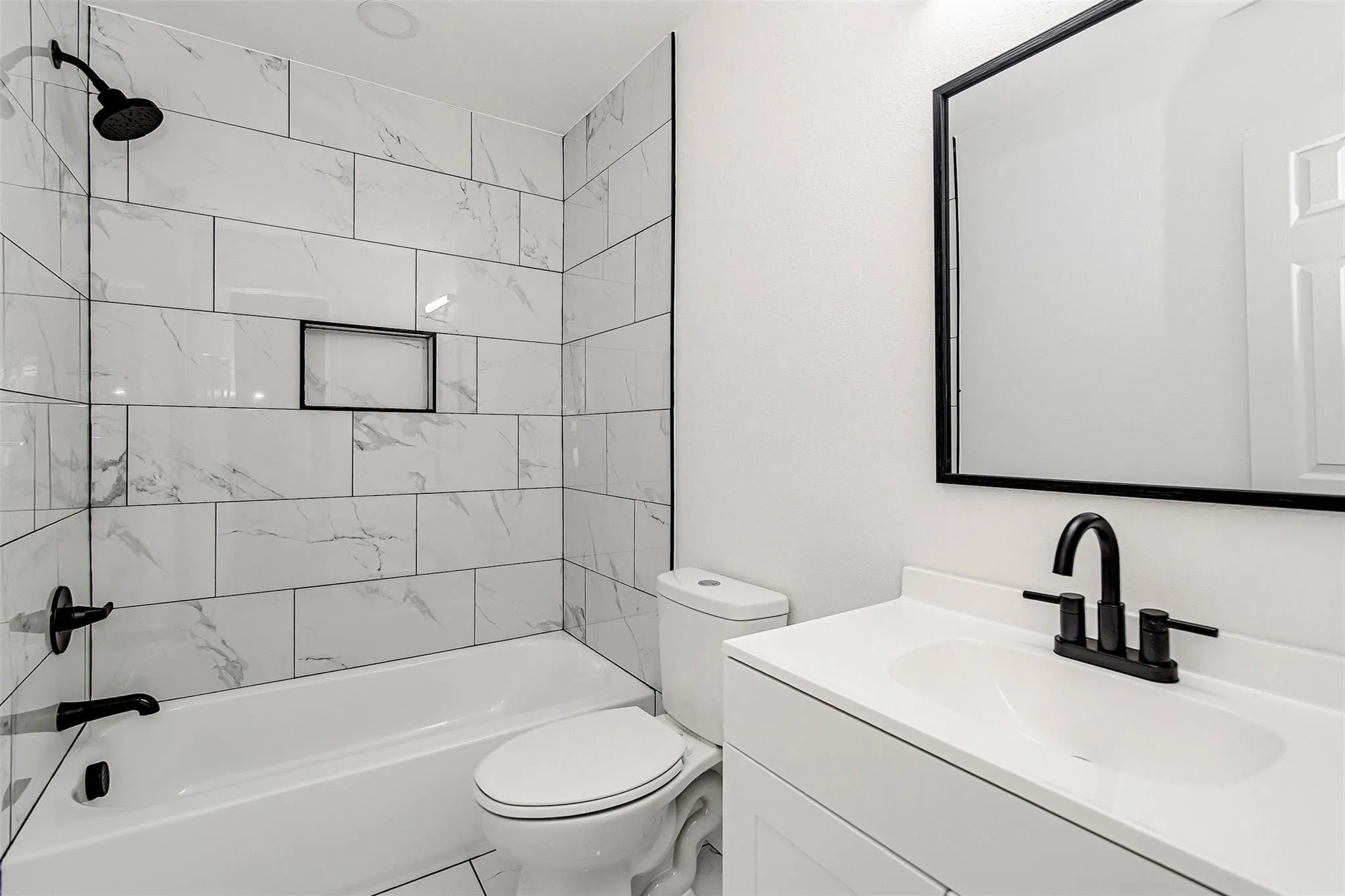 Contemporary vanity with white countertop and integrated sink, matte black faucet, framed mirror, and subway tile shower surround with recessed niche