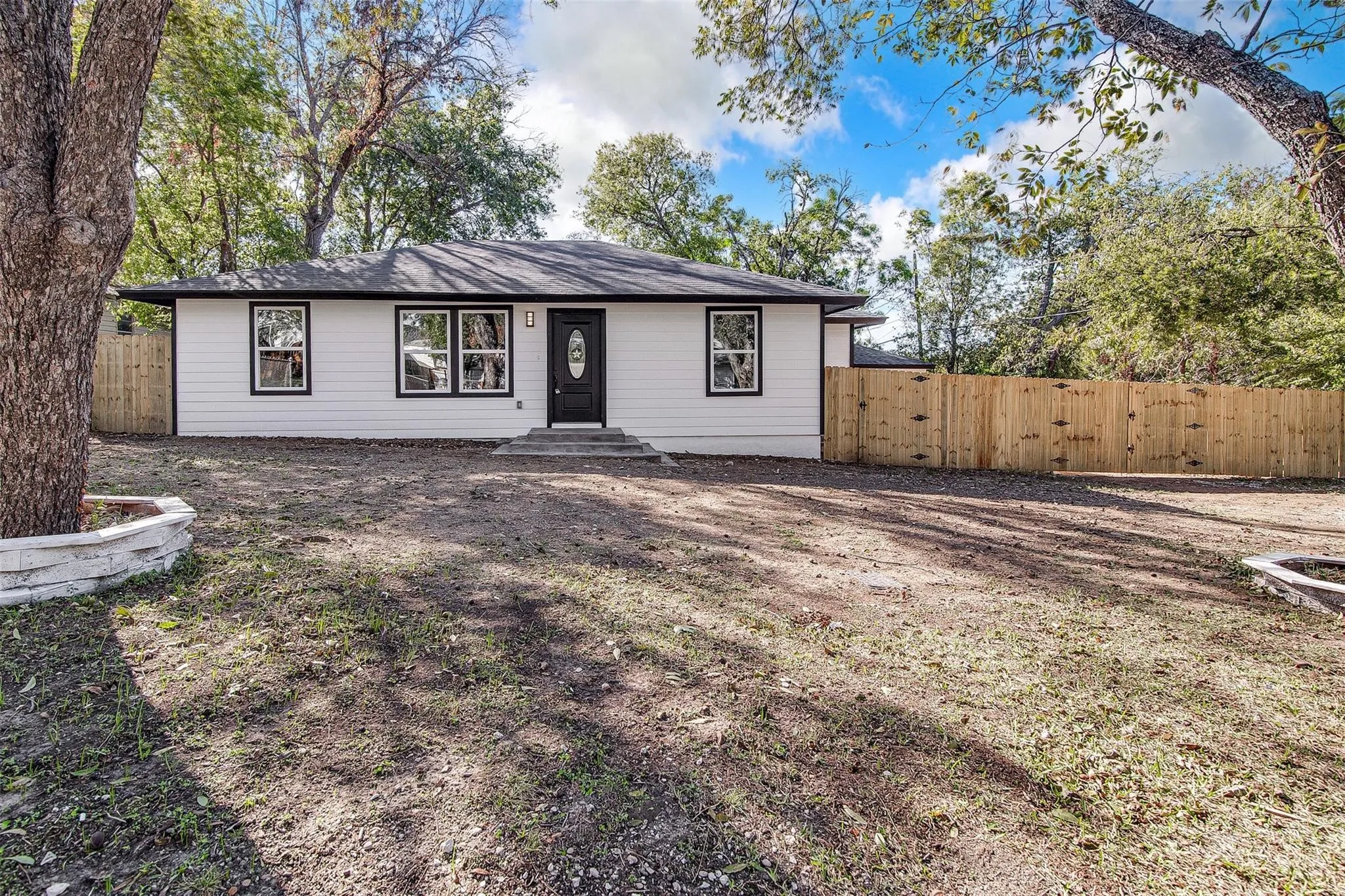 White exterior siding, black-trimmed windows, black entry door, and a wood privacy fence