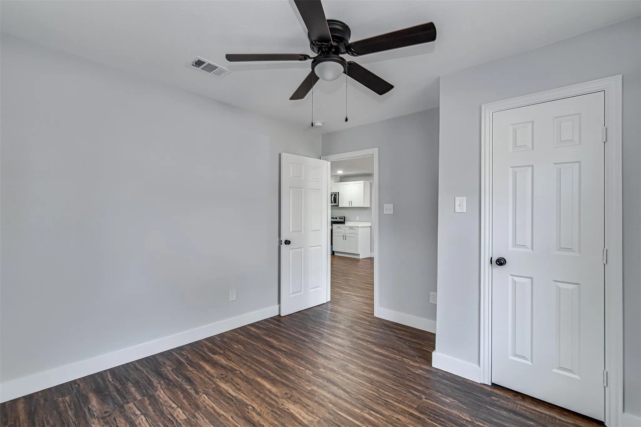 Wood-finish flooring, light gray wall tones, a ceiling fan with light, and white paneled doors