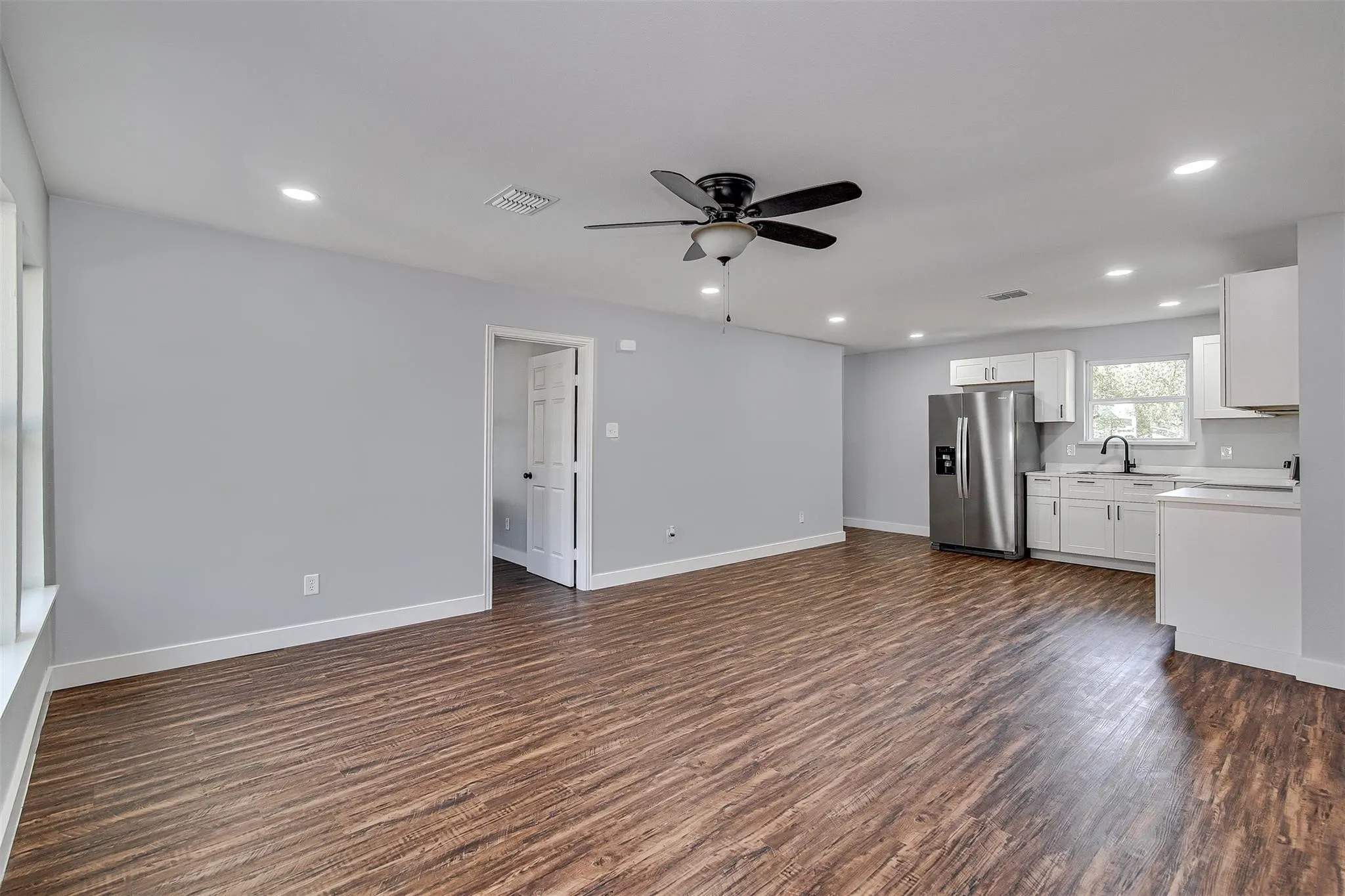 Wood-finish flooring, recessed lighting, ceiling fan with light, white kitchen cabinetry, and stainless steel refrigerator