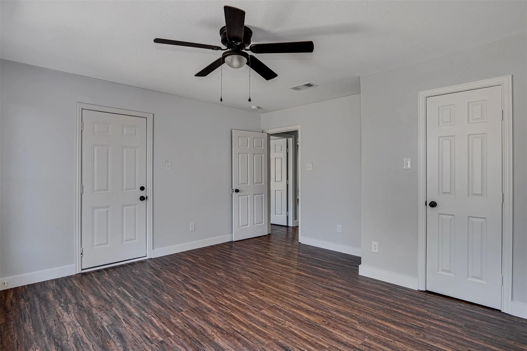 Wood-finish flooring, white panel doors, and a ceiling fan with integrated lighting