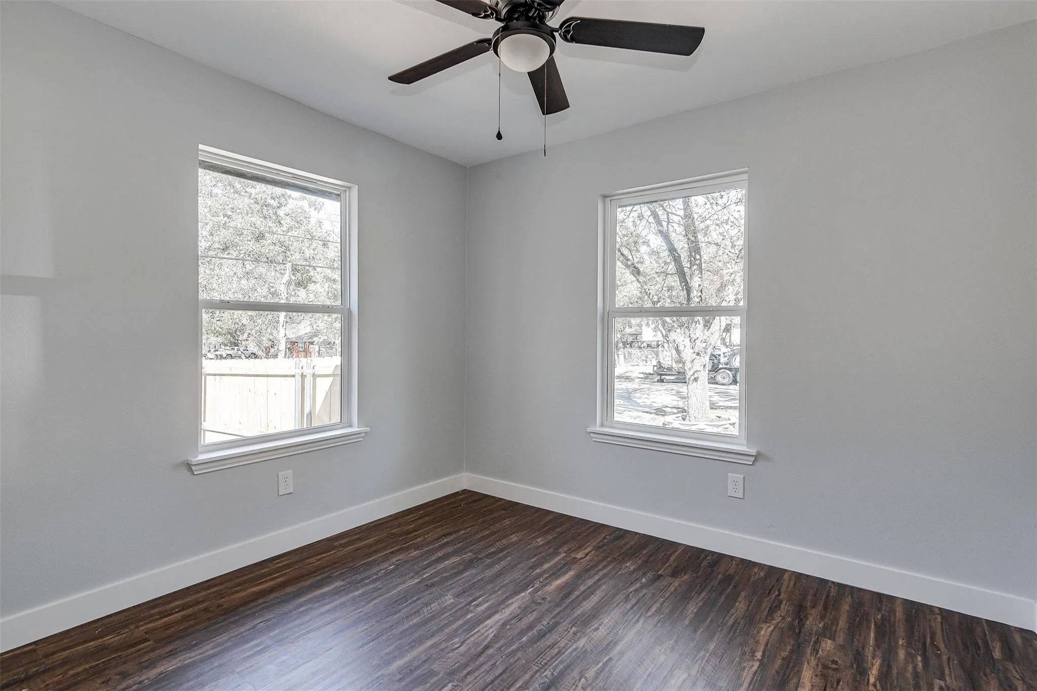 Neutral wall color, wood-finish flooring, white window trim, dual windows, and a ceiling fan with integrated lighting
