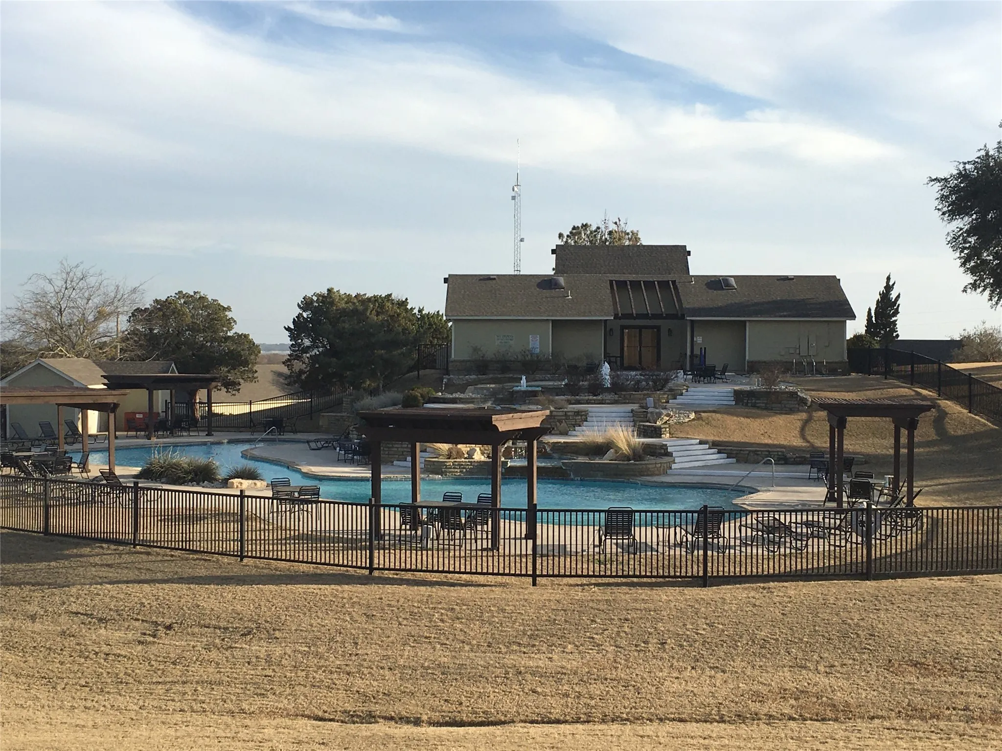 Expansive outdoor pool area featuring a resort-style swimming pool, multiple pergolas, and a decorative water feature