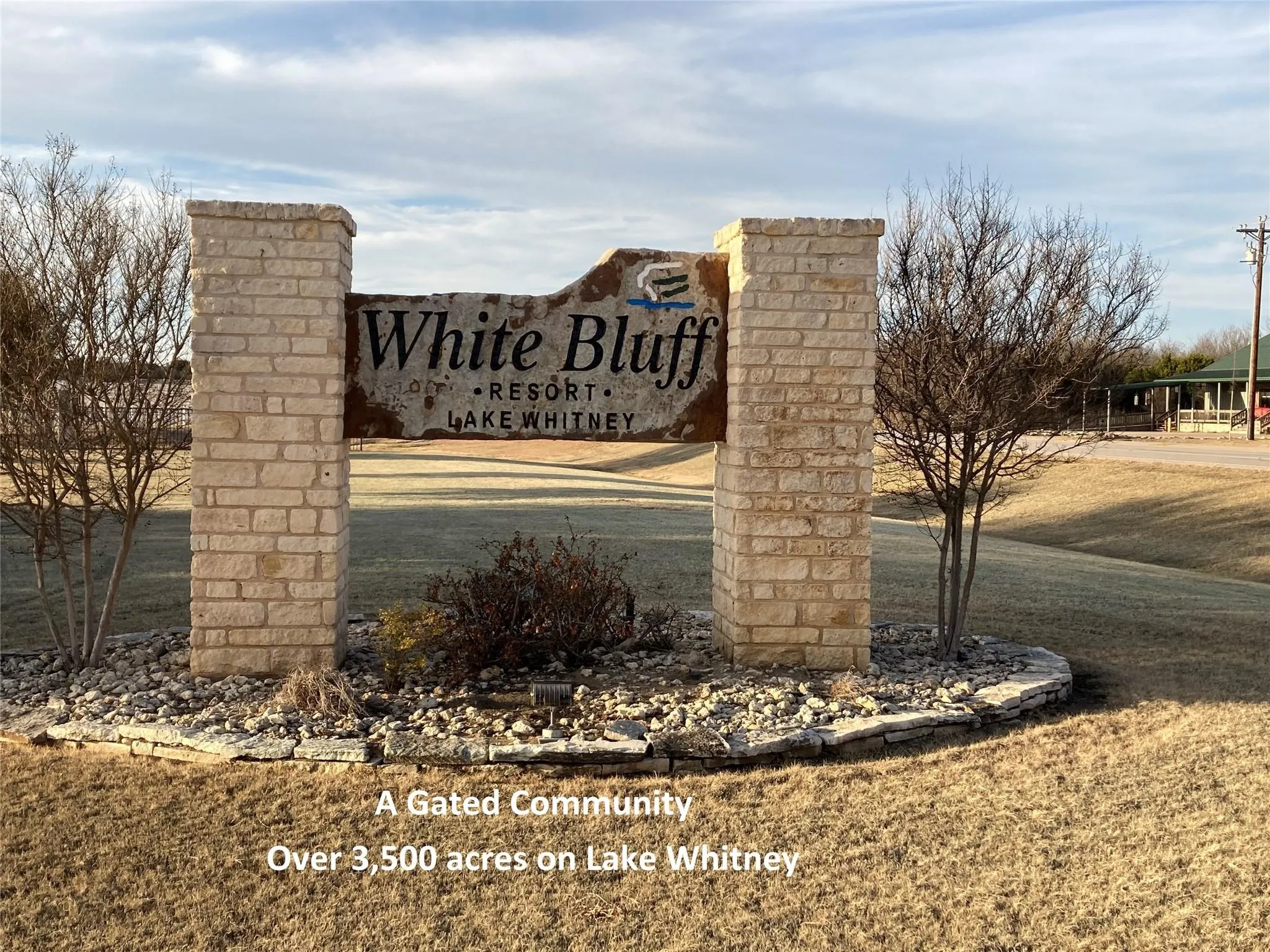 Stone column entrance featuring a rustic sign, landscaped with decorative rock and plantings