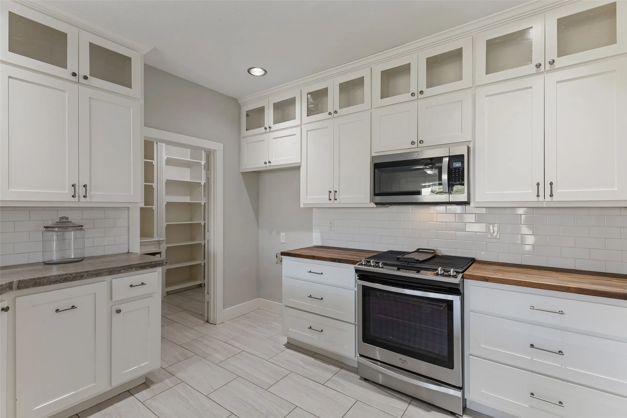 White shaker-style cabinetry with upper glass-front cabinets, stainless steel appliances and brand new butcher block countertops