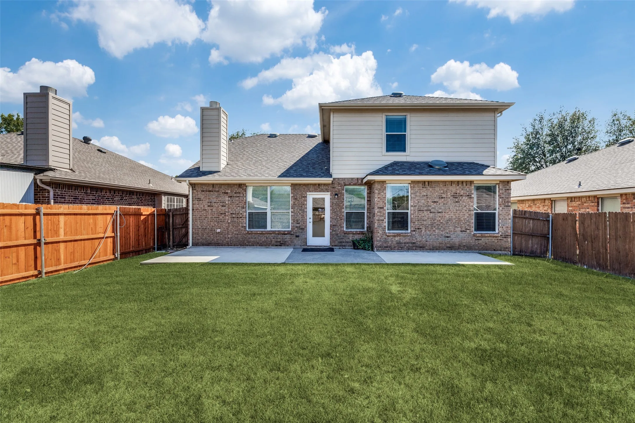 Expansive backyard featuring a manicured lawn, full privacy fencing, and a concrete patio