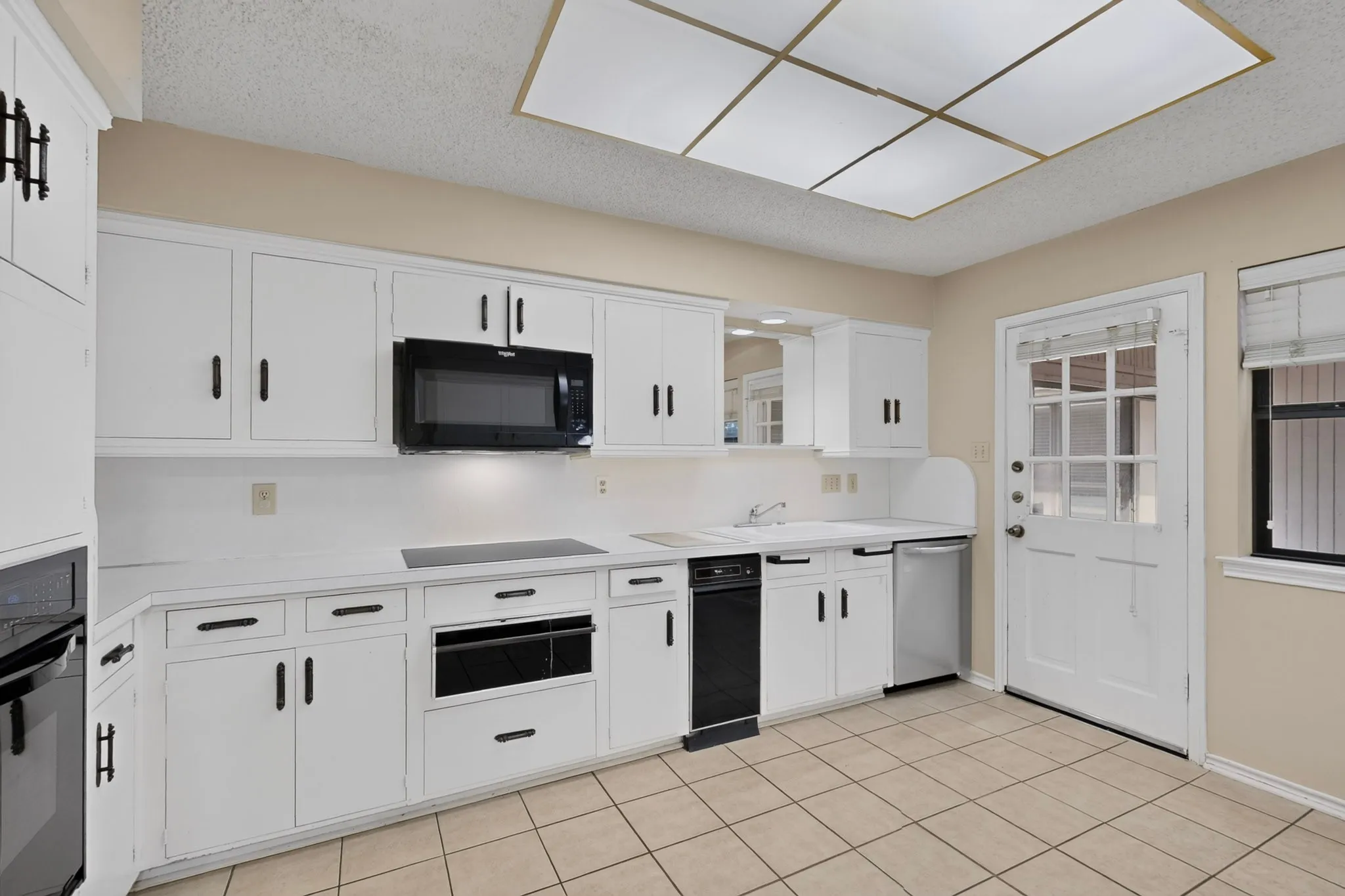 White cabinetry with matte black hardware, integrated black appliances, tiled flooring, built-in microwave, and a glass-paned exterior door
