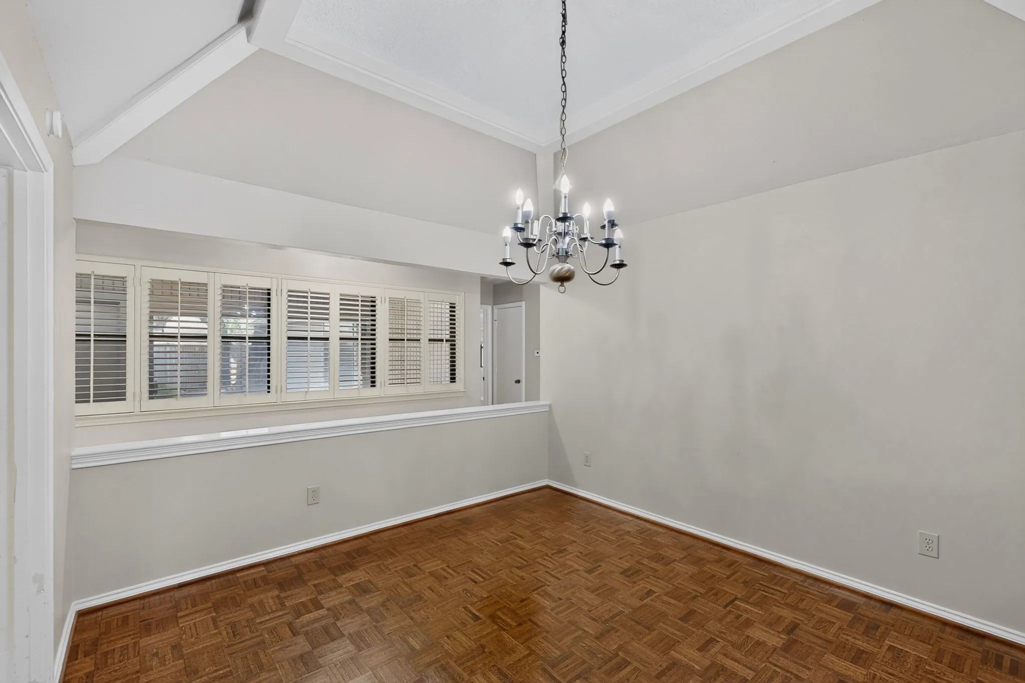 Vaulted ceiling with exposed beam, chandelier lighting, parquet wood-finish flooring, and upper-level windows with plantation shutters