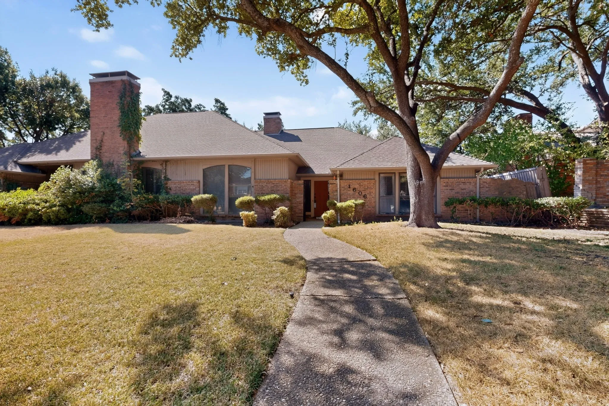 Single-story brick exterior with a pitched roof, front entry pathway, mature trees, and established landscaping