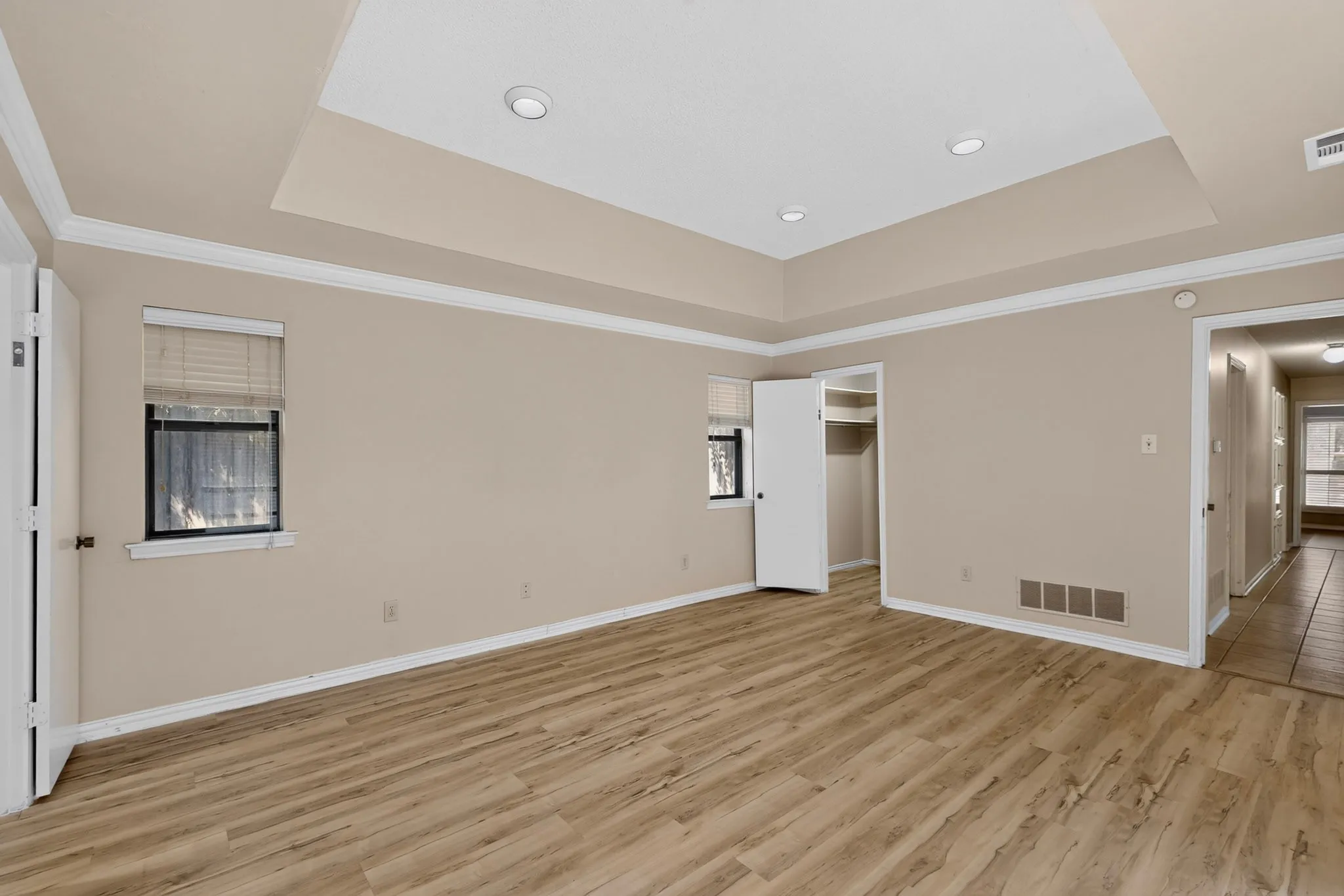 Recessed tray ceiling, crown molding, wood-finish flooring, two windows, and an open closet with shelving