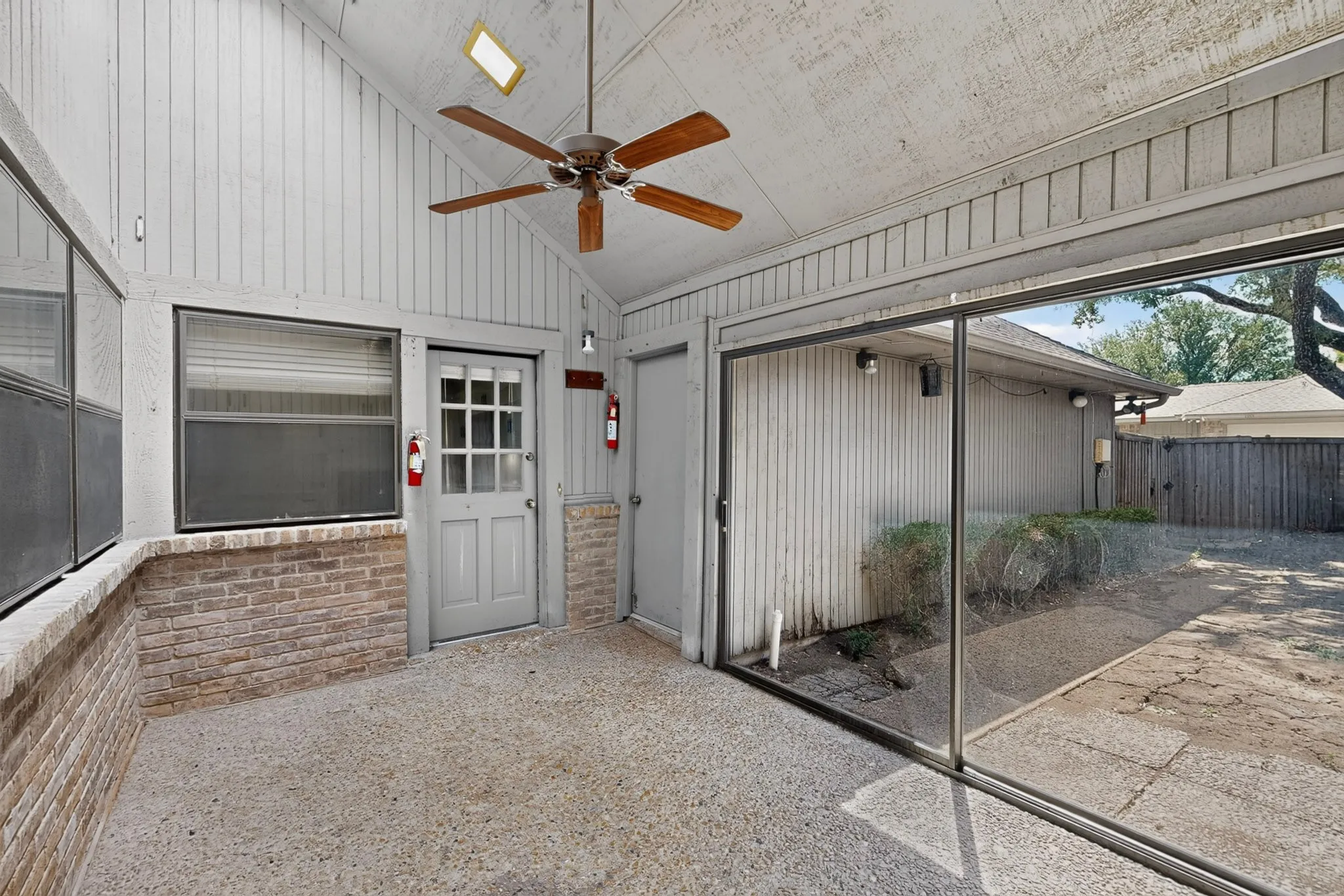 Enclosed patio featuring a vaulted ceiling, exposed aggregate flooring, brick wainscoting, and a ceiling fan with light
