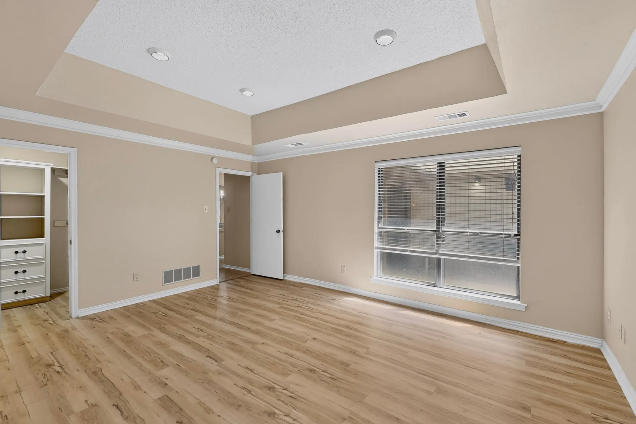 Recessed lighting, crown molding, a tray ceiling, wood-finish flooring, and built-in closet shelving