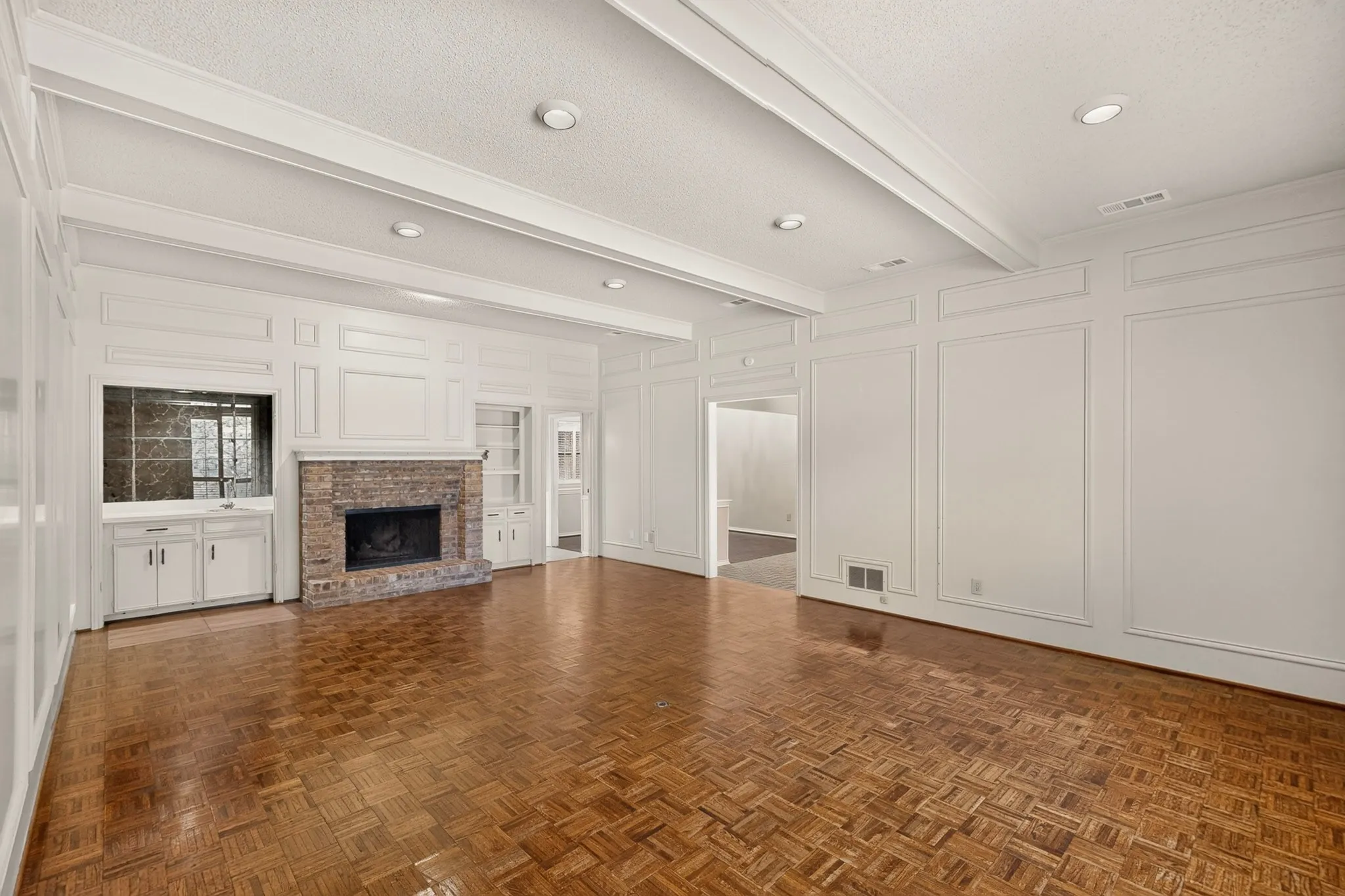 Wood-finish flooring, brick fireplace, built-in cabinetry, recessed lighting, and decorative wall paneling