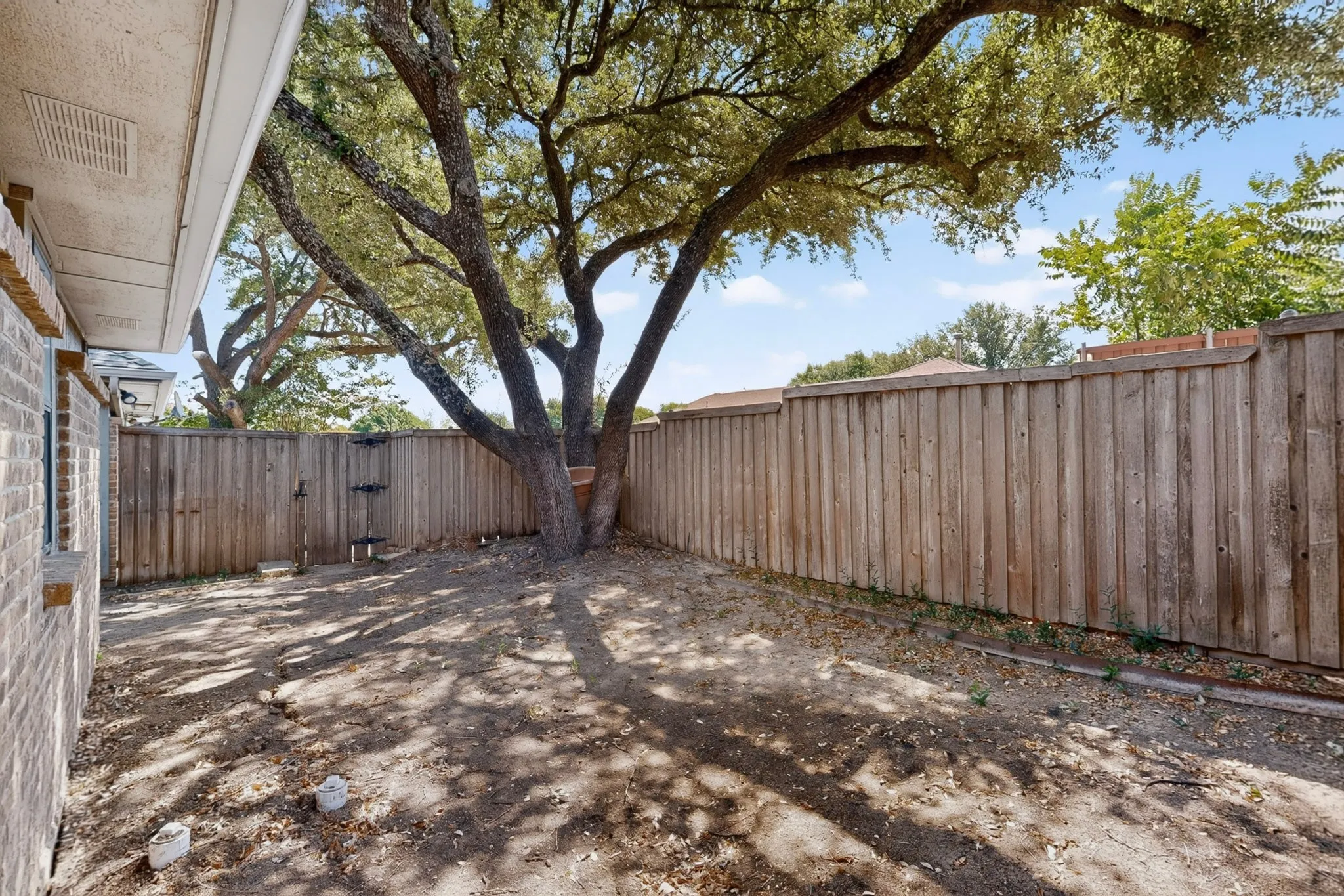 Private backyard space featuring a mature shade tree, a wood privacy fence, and a brick exterior wall