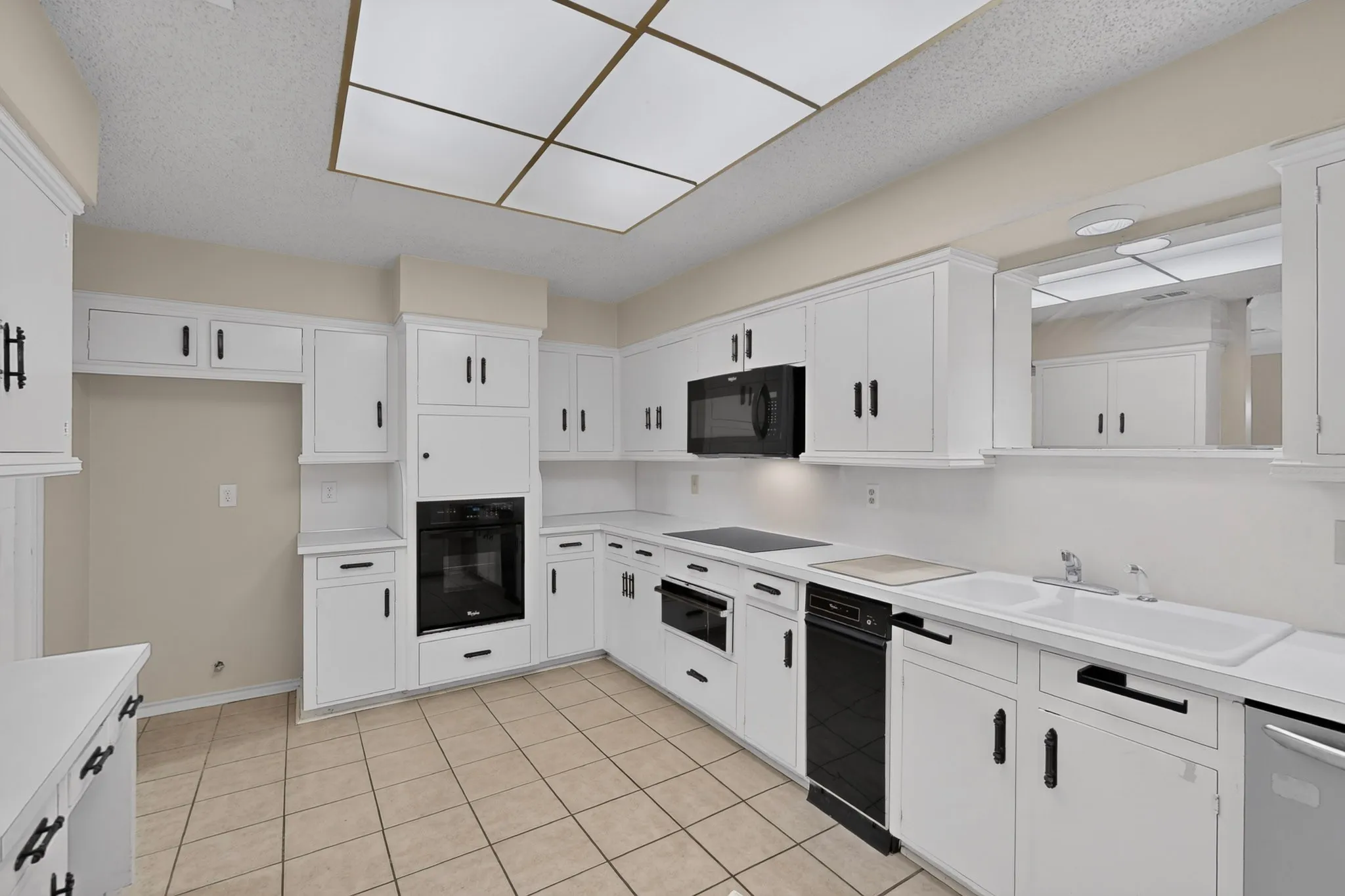 Kitchen featuring white cabinetry, black hardware, built-in appliances, ceramic tile flooring, and a drop-in sink