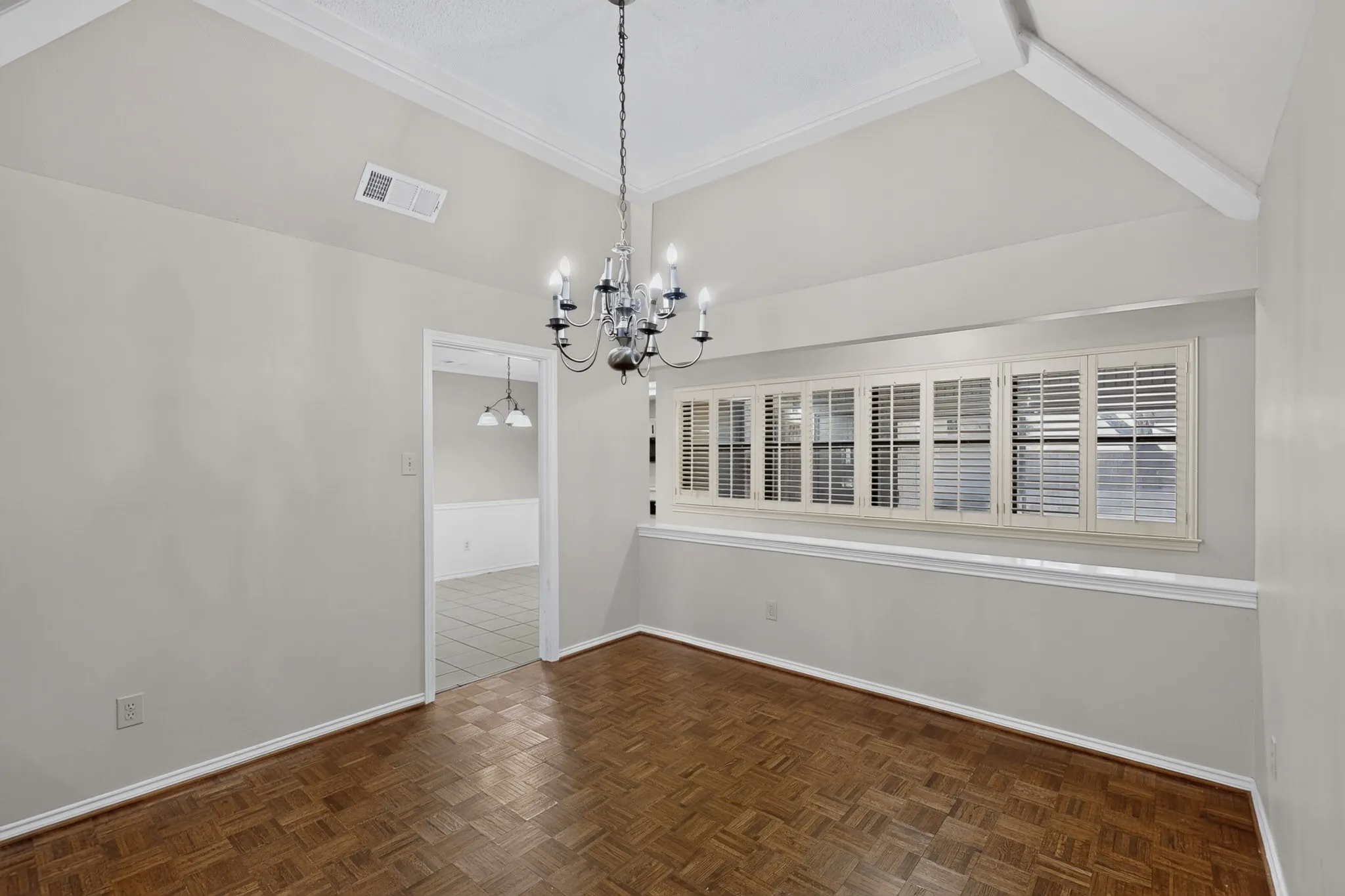 Elegant dining room showcasing soaring vaulted ceilings with crown molding, herringbone wood-finish flooring, and a striking multi-arm chandelier