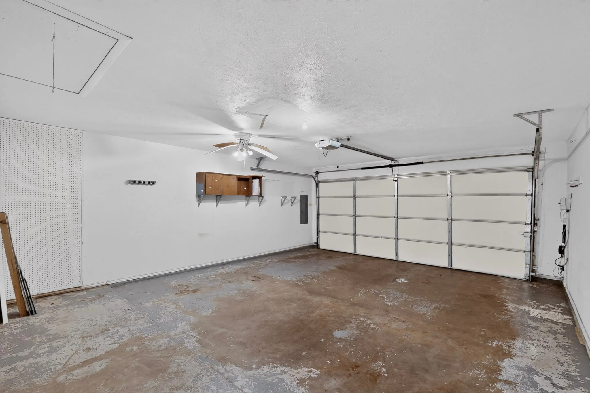 Single-bay garage with an overhead door, built-in shelving, and a ceiling fan
