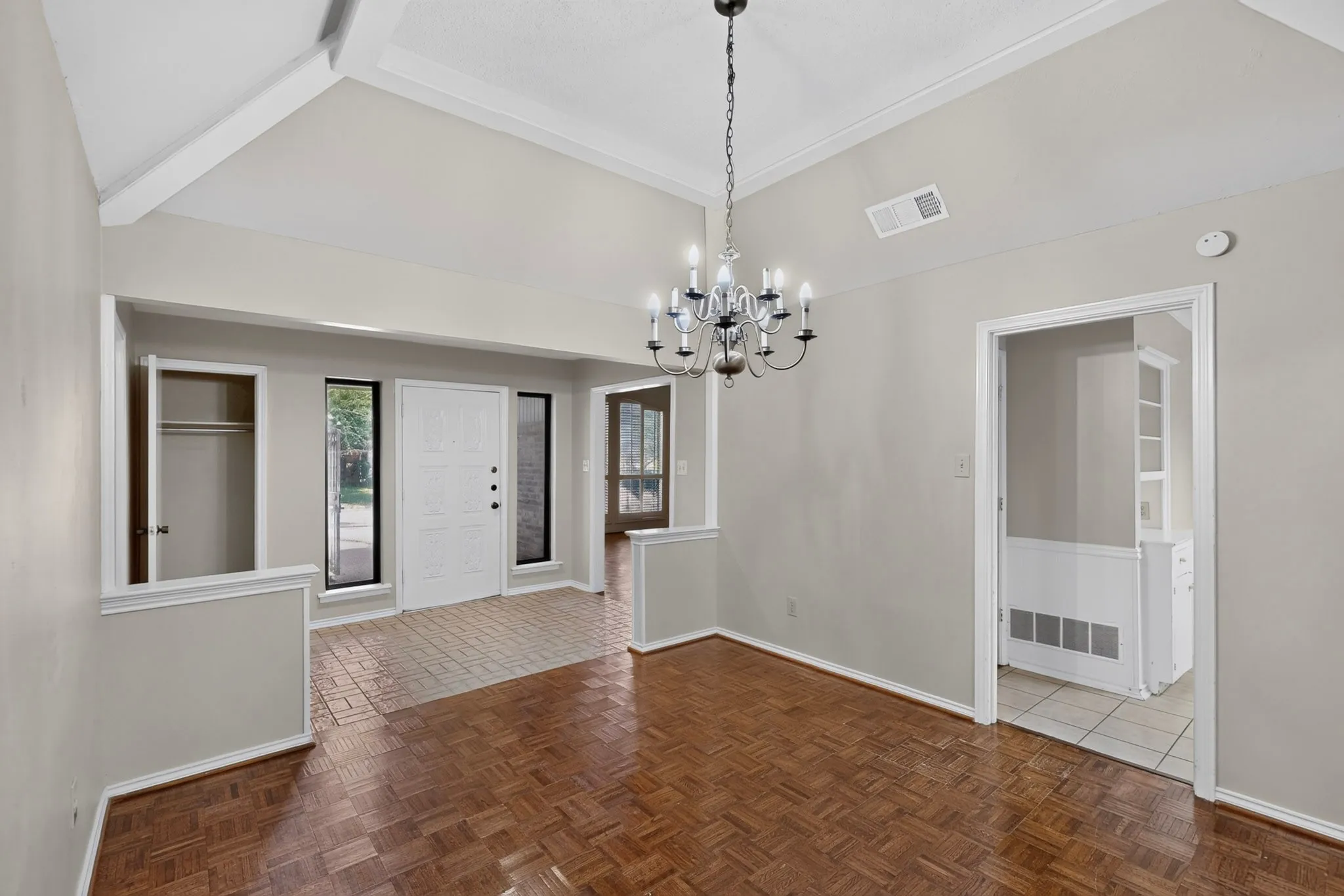 Vaulted ceiling with exposed beams, wood-finish flooring, white paneled entry door, recessed entry, and an elegant chandelier